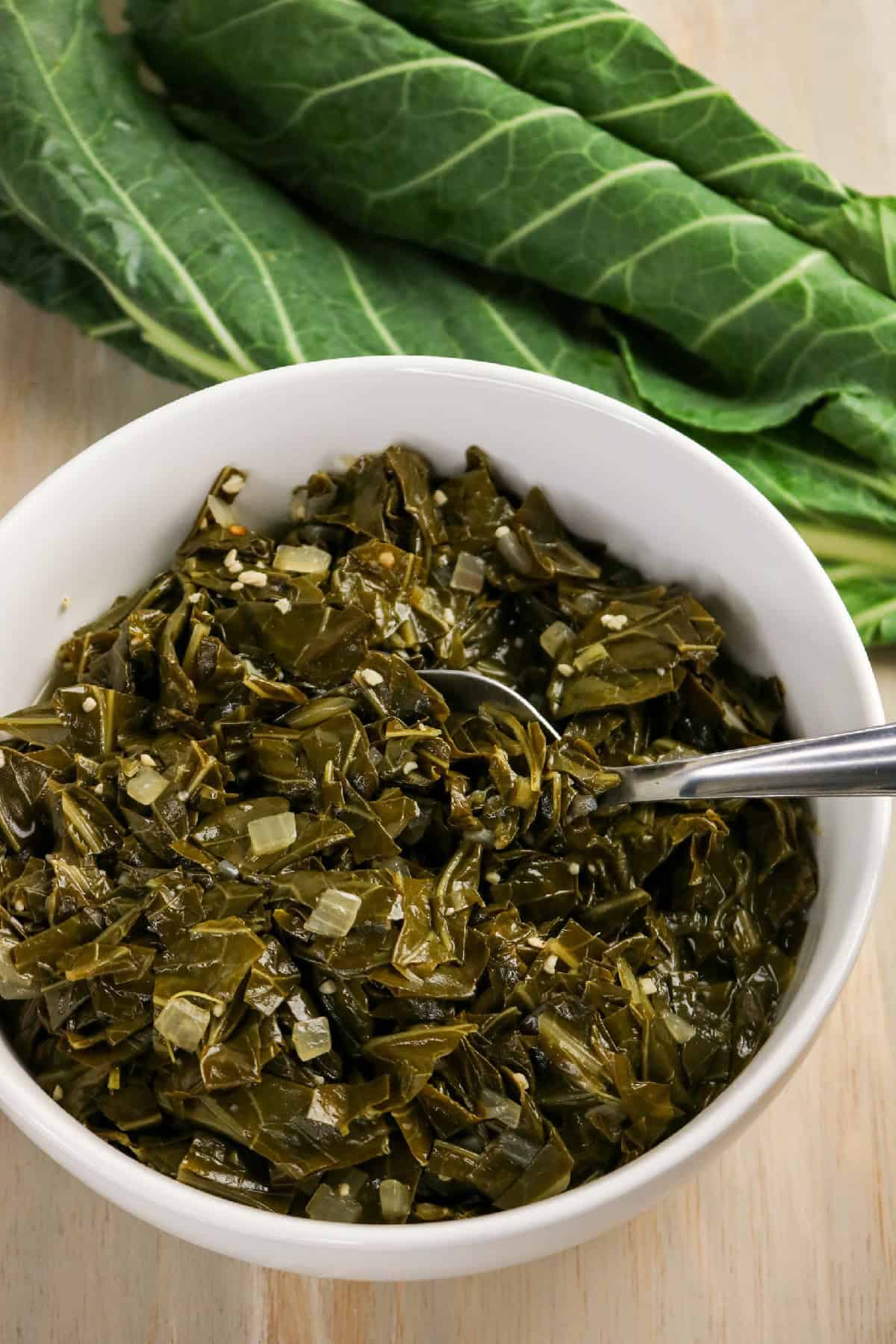 Close-up of braised collard greens with visible onion pieces and seasoning.