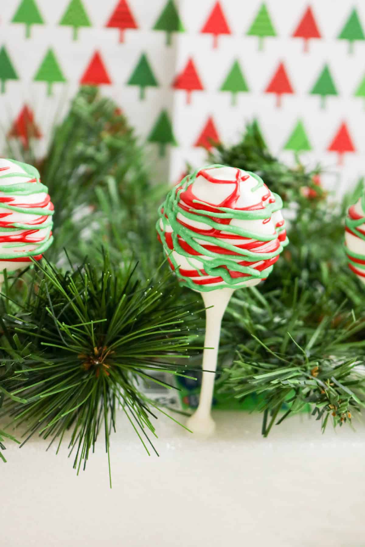 Christmas cake pop with red and green drizzle on white chocolate, set in festive greenery.