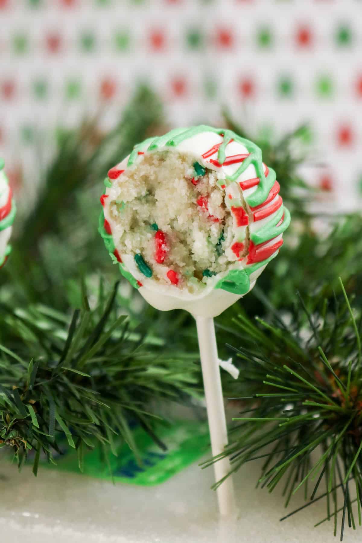 Bitten Christmas cake pop showing vanilla cake and sprinkles inside white chocolate coating.