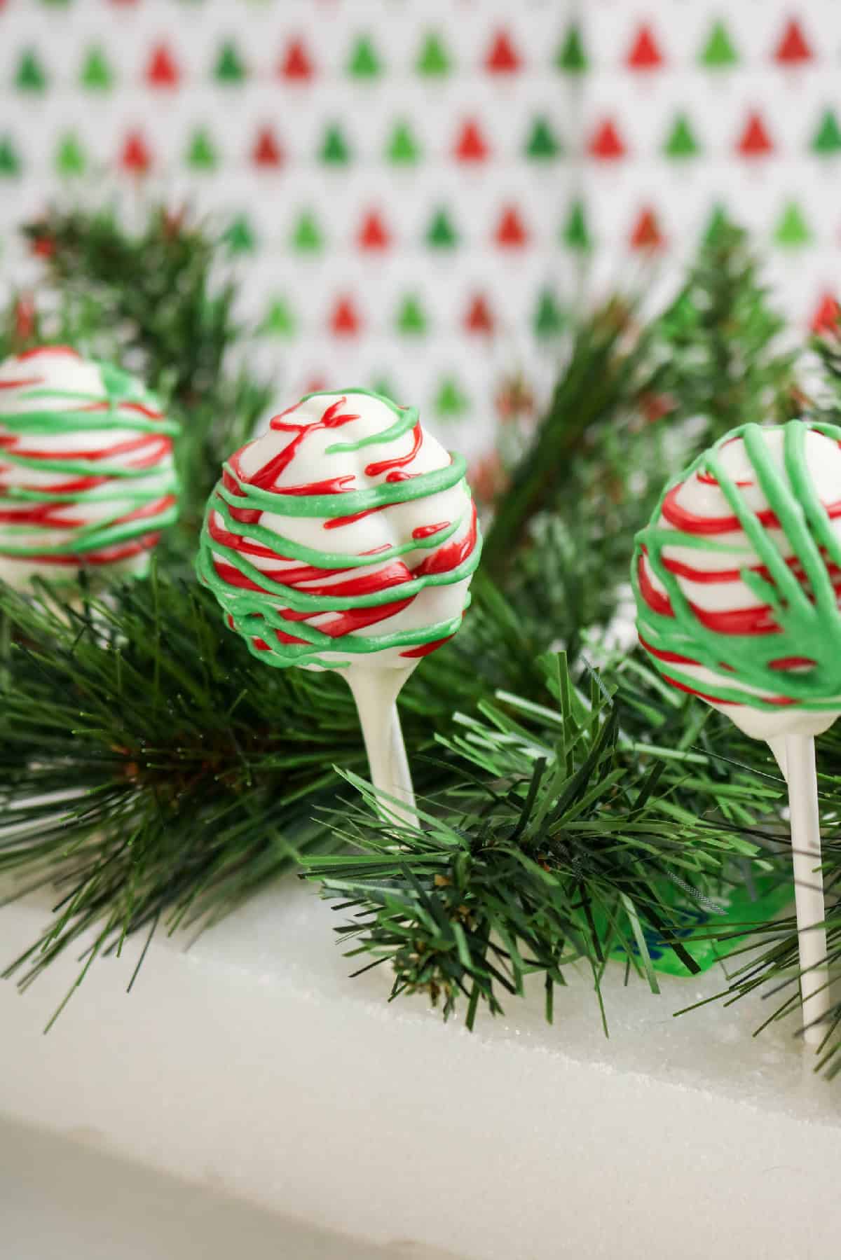 Three Christmas cake pops with red and green drizzle arranged on pine garland.