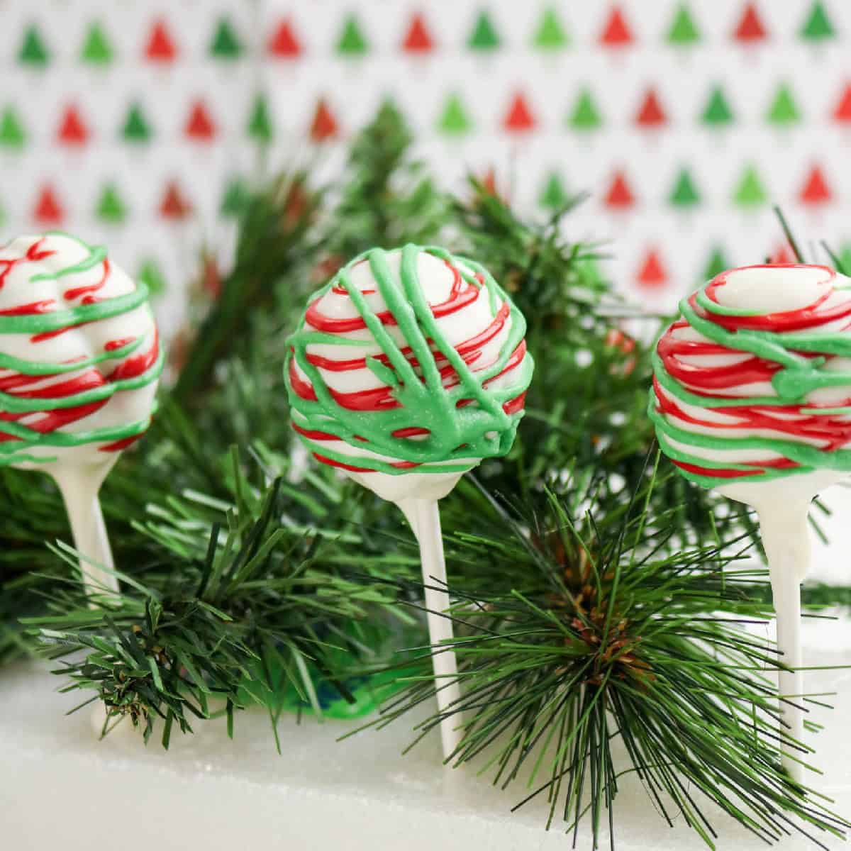 Christmas cake pops decorated with red and green drizzle on white chocolate coating.