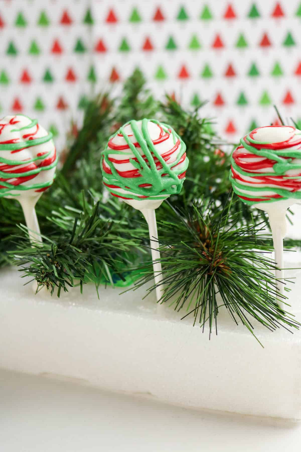 Close-up of a Christmas cake pop covered in white chocolate with red and green drizzle.