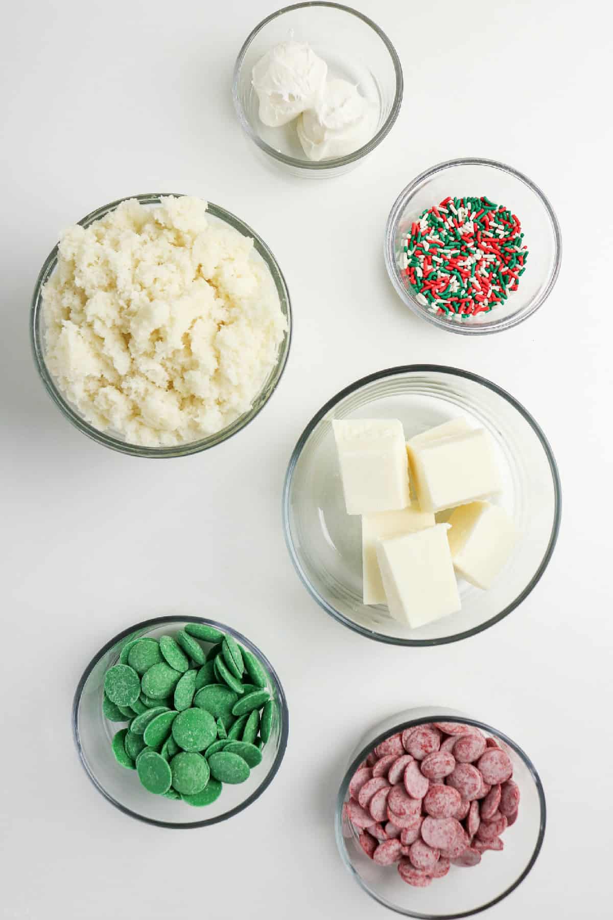 Bowls of crumbled vanilla cake, white chocolate, red and green candy melts, and holiday sprinkles for making Christmas cake pops.