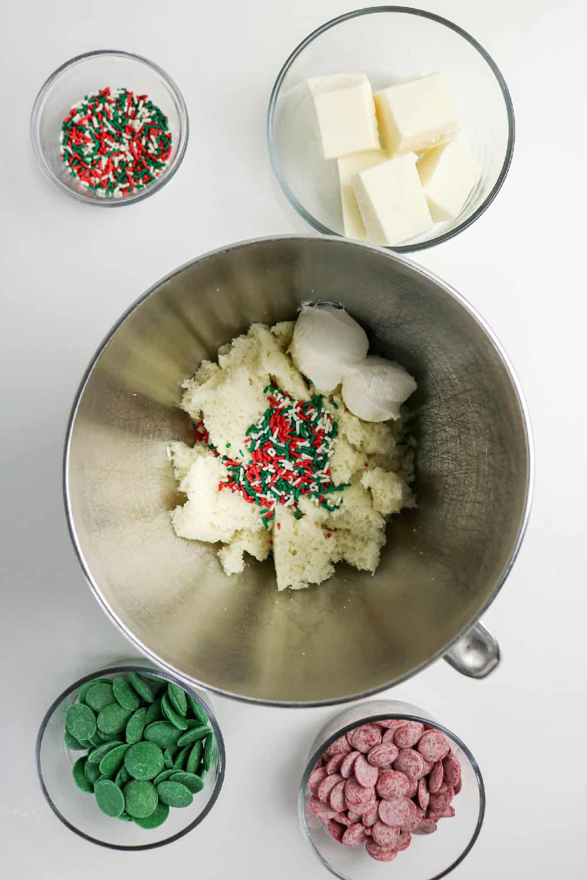 Crumbled cake, frosting, and Christmas sprinkles added to a mixing bowl for cake pop dough.