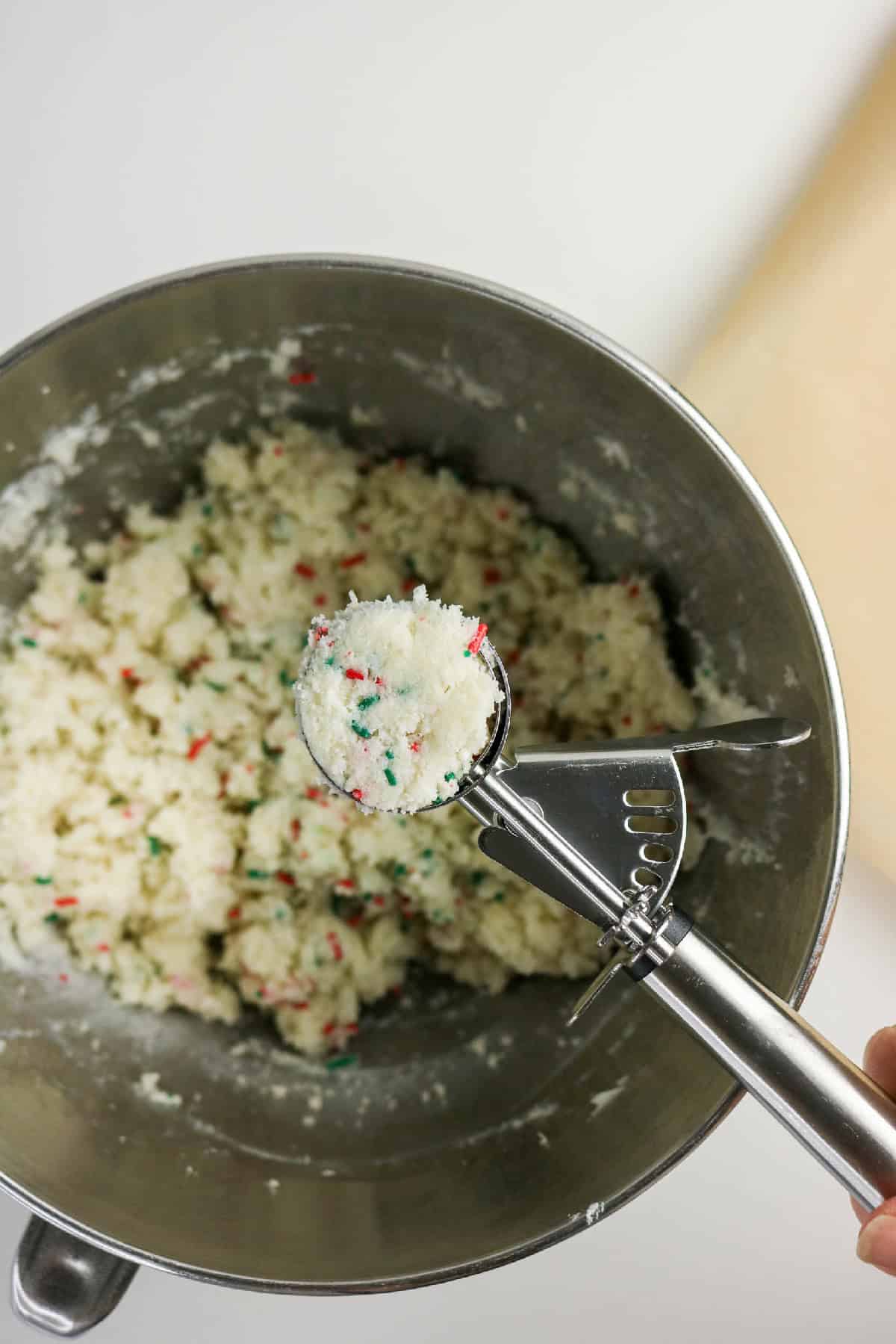 Cookie scoop holding a portion of Christmas cake pop dough over a mixing bowl.