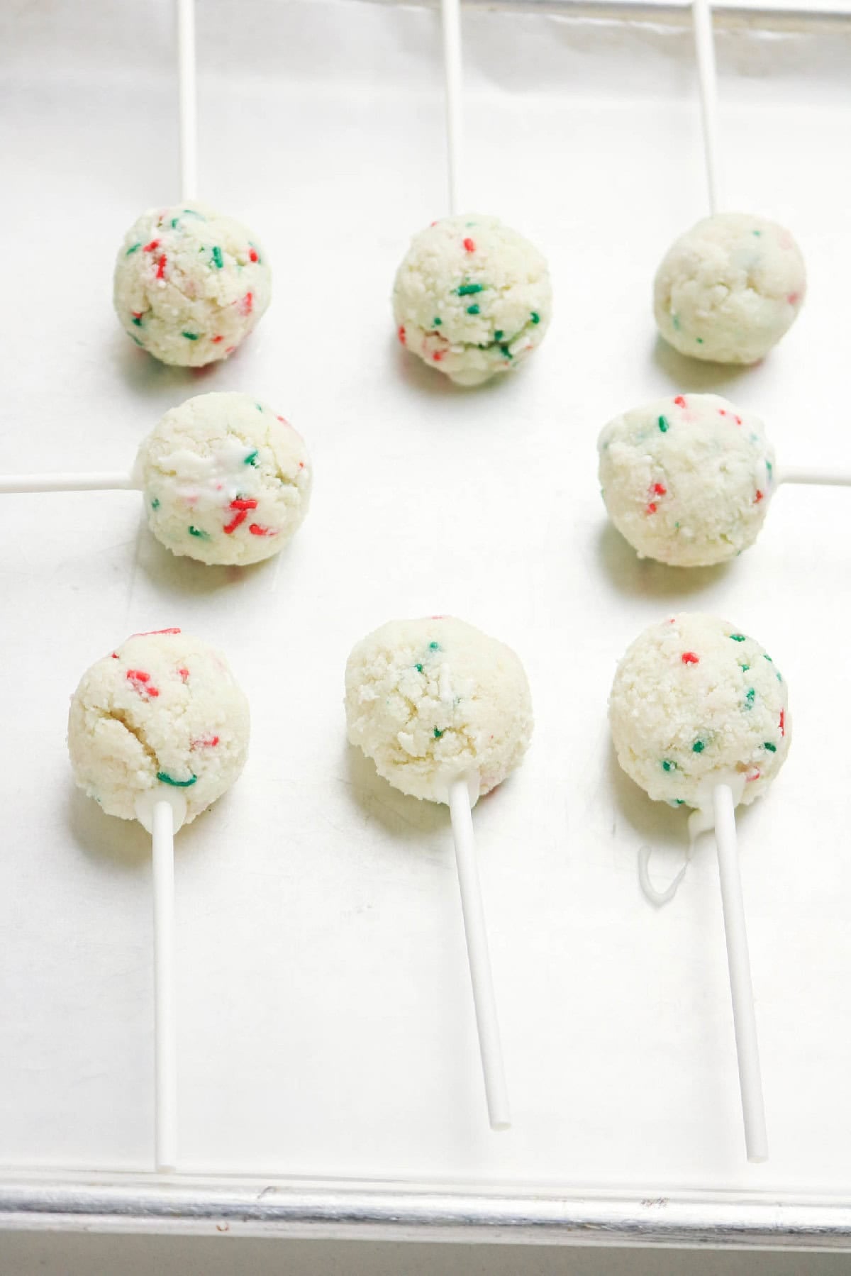 Cake pop balls with sticks inserted and resting on a baking tray before dipping.