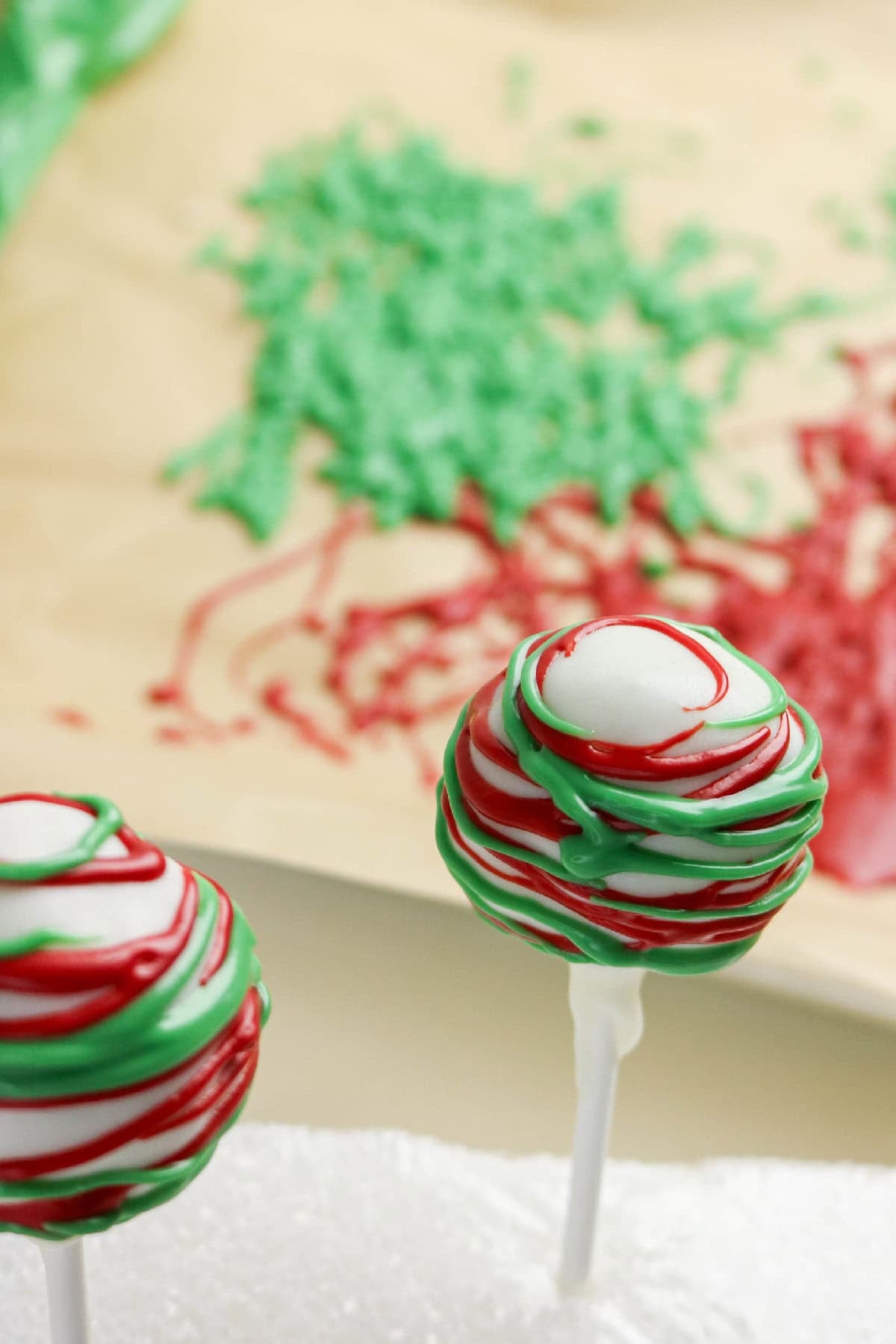 Christmas cake pops decorated with red and green drizzle on white chocolate coating.