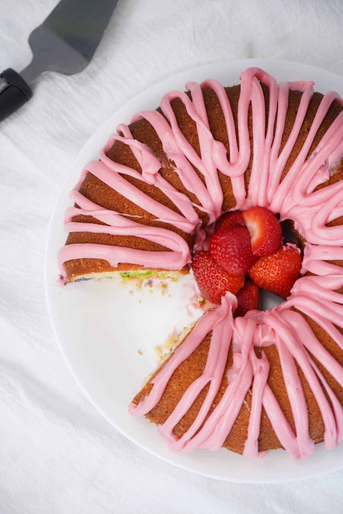 Sliced Easter bundt cake with pink icing and fresh strawberries on a white plate.