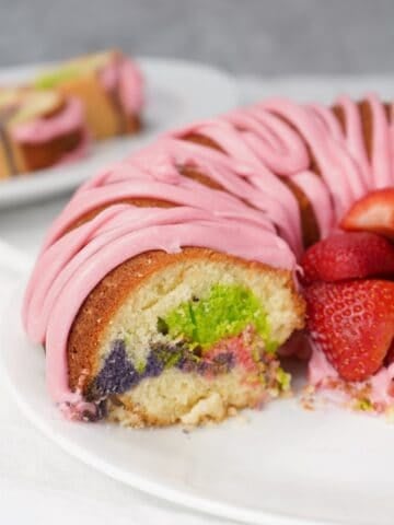 Slice of Easter Bundt cake with pink glaze and colorful marble crumb, served with fresh strawberries.