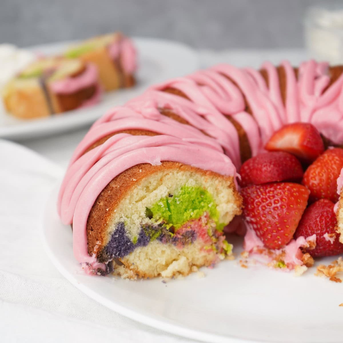 Slice of Easter Bundt cake with pink glaze and colorful marble crumb, served with fresh strawberries.