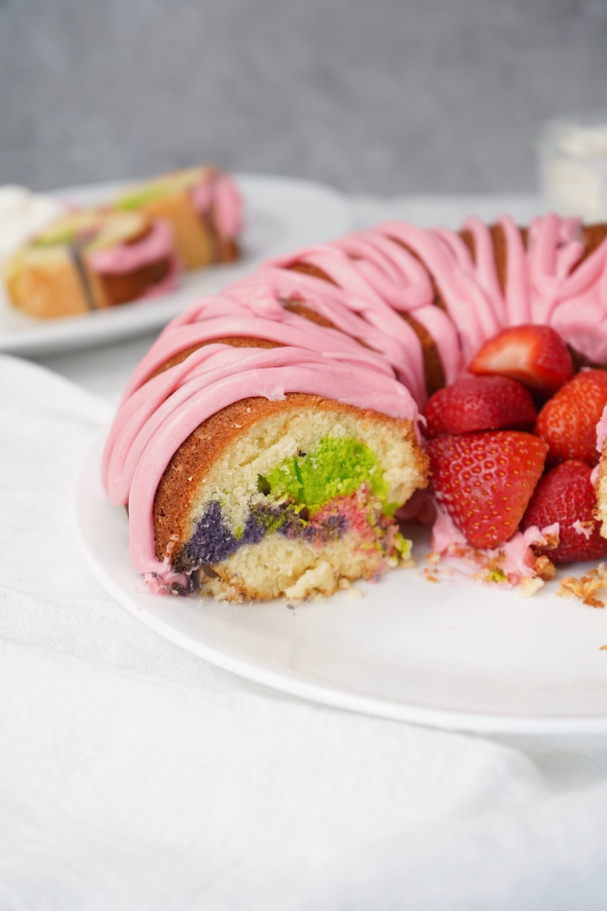 Easter bundt cake slice with pink icing and strawberries, whole cake in the background.