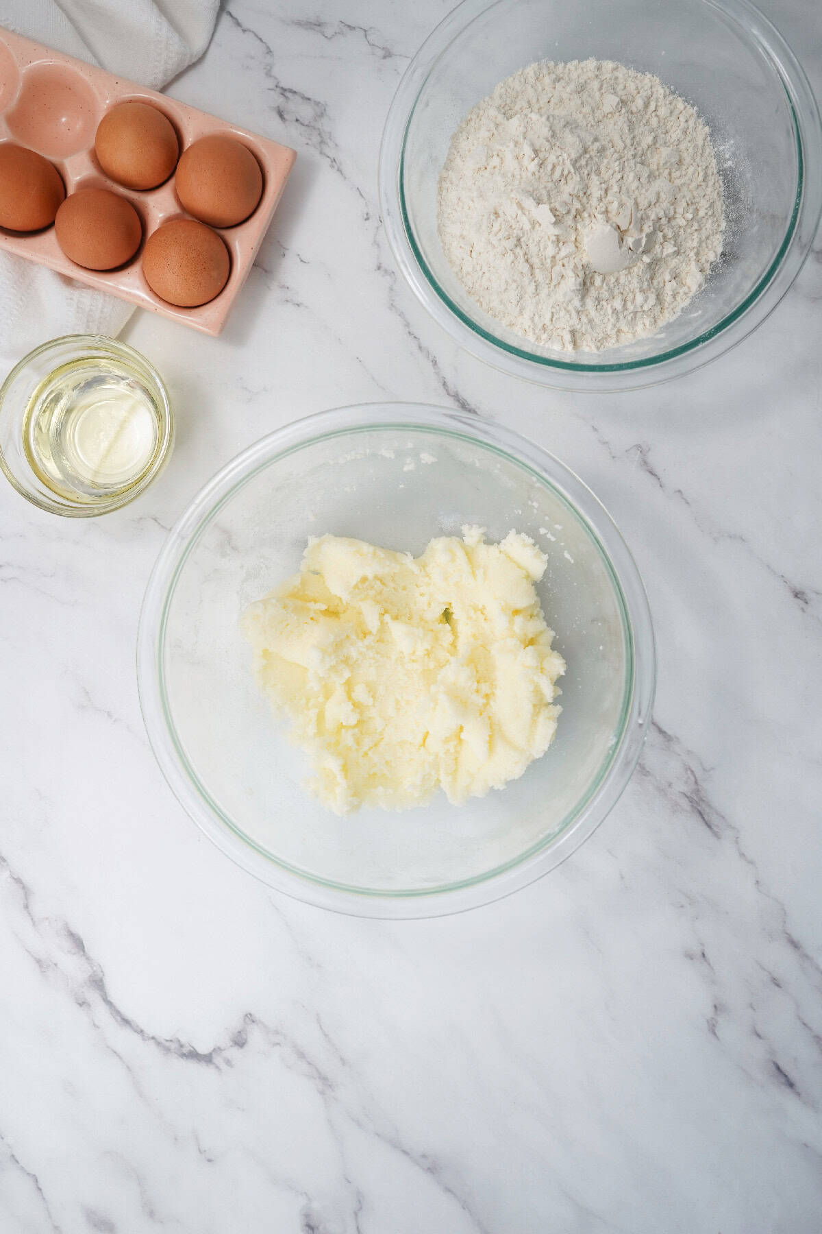 Ingredients for Easter bundt cake including eggs, flour, oil, and softened butter on a marble countertop.