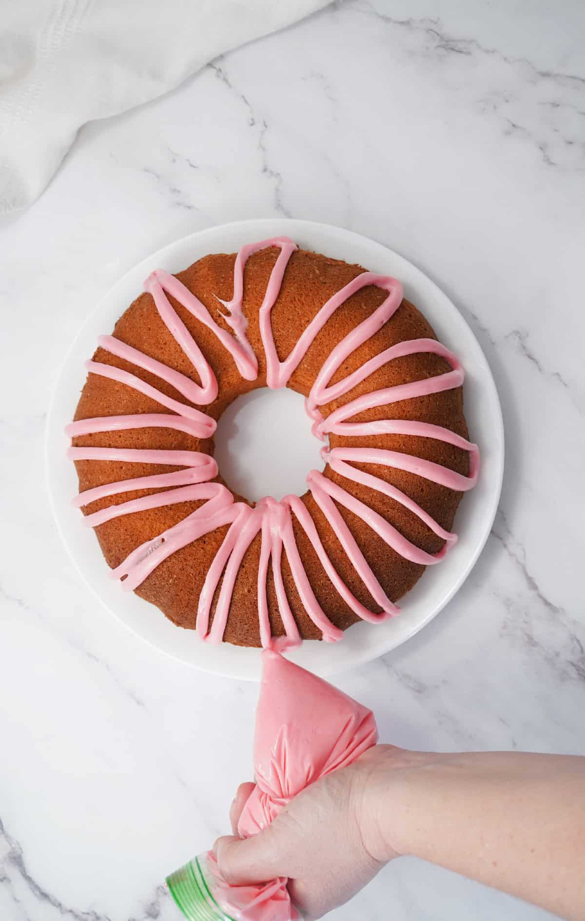 Pink icing being drizzled over a baked Easter bundt cake on a white plate.