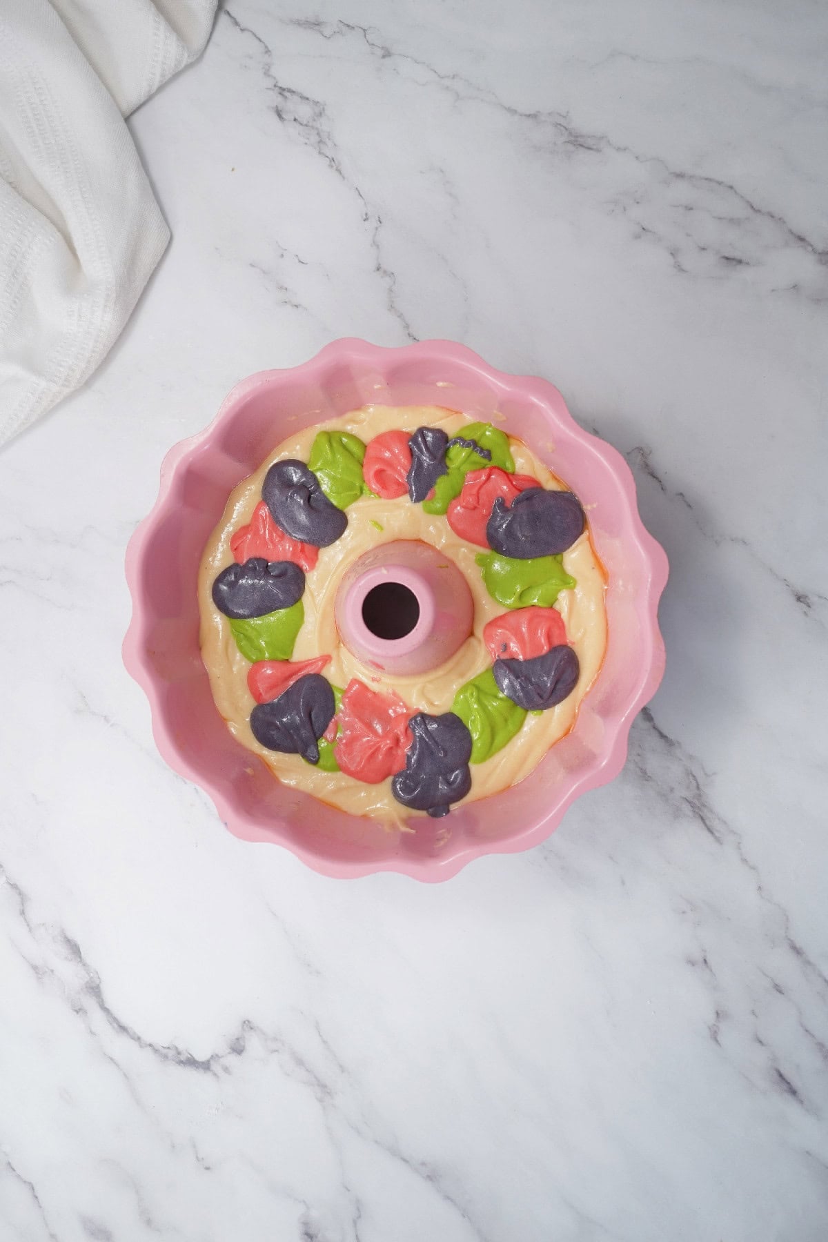 Colored cake batter spooned into a pink bundt pan for a marbled Easter cake.