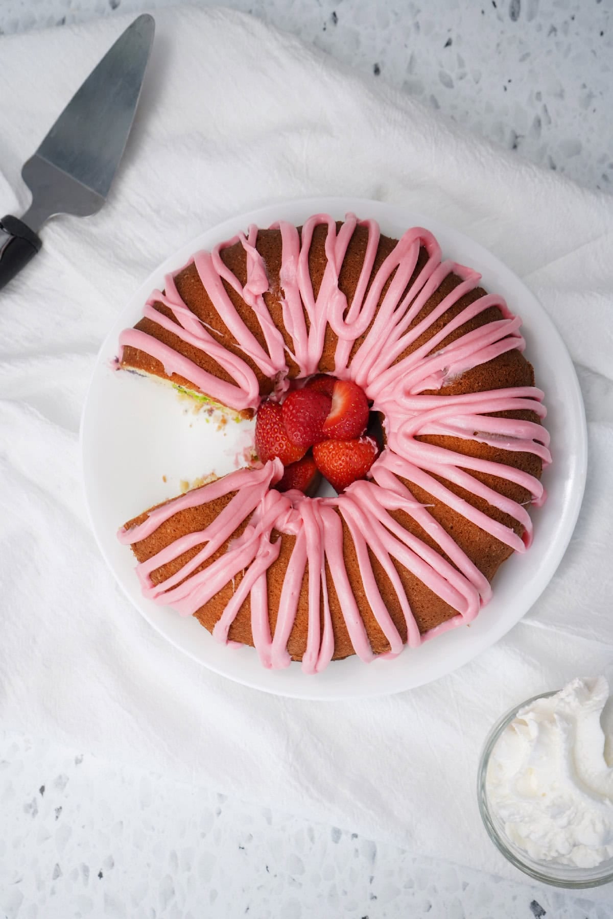 Sliced Easter bundt cake with pink icing and fresh strawberries on a serving plate.