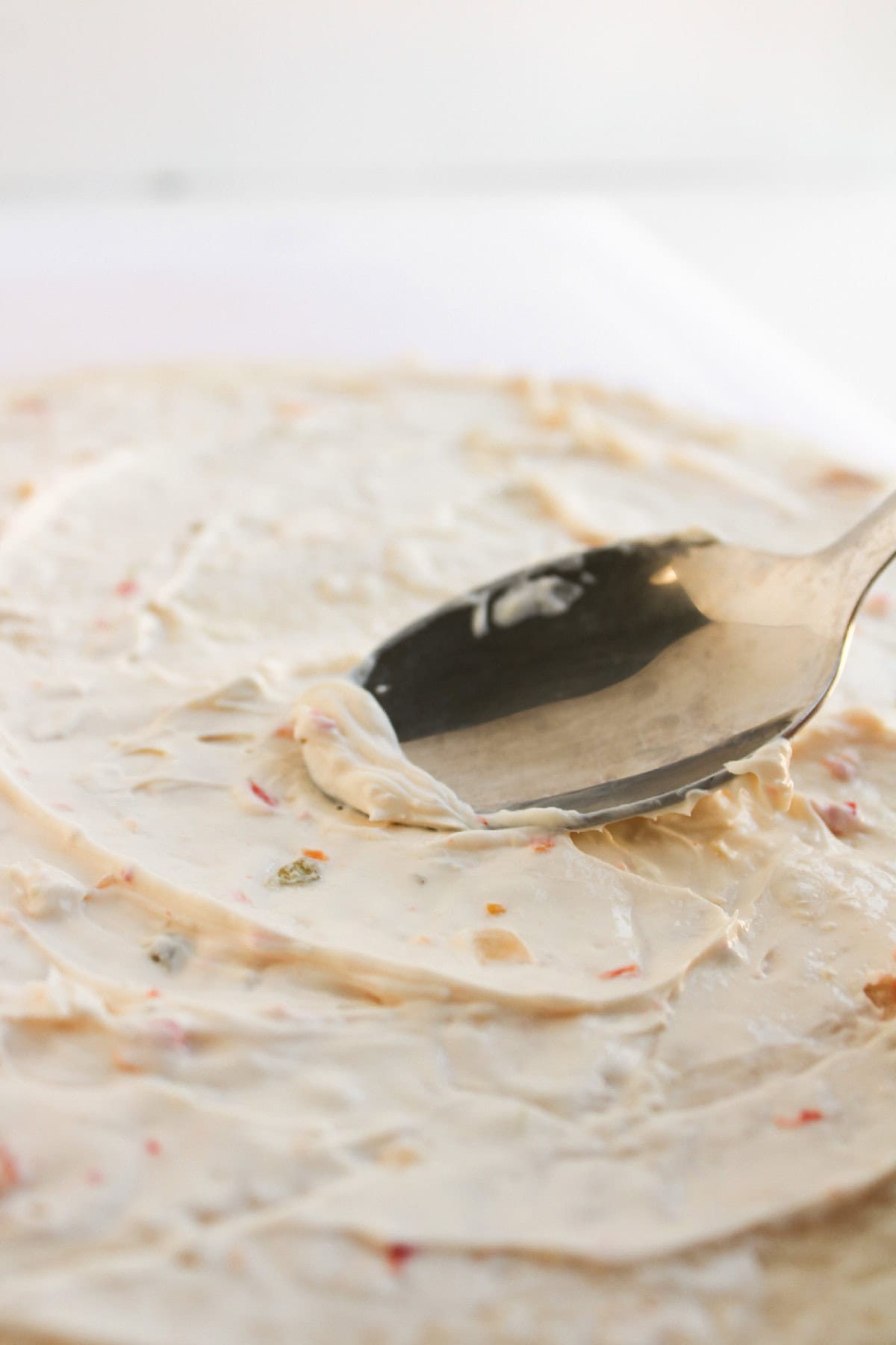 Creamy vegetable spread being smoothed over a flour tortilla with a spoon.