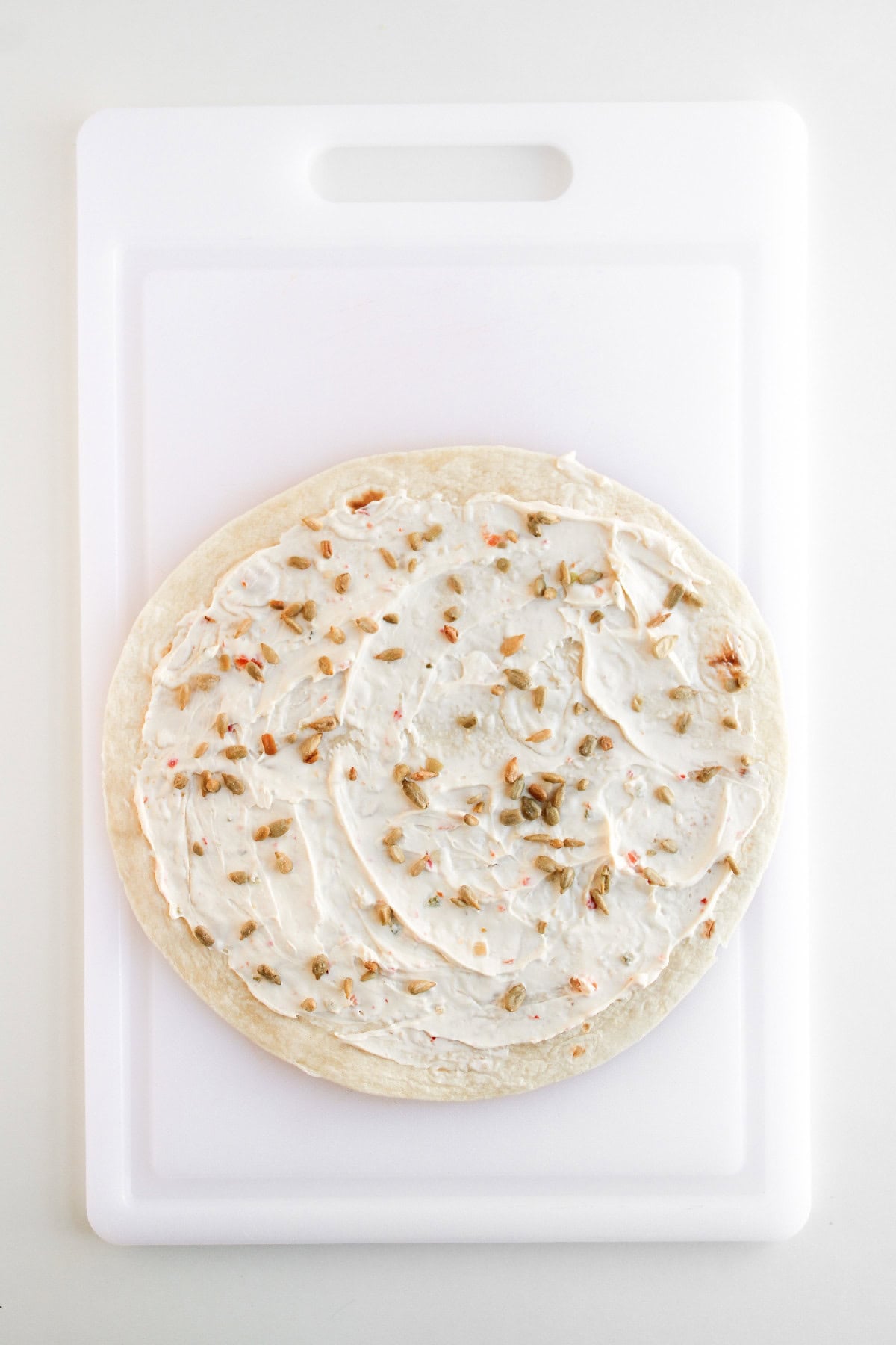 Tortilla topped with creamy spread and sprinkled seeds before adding vegetables.