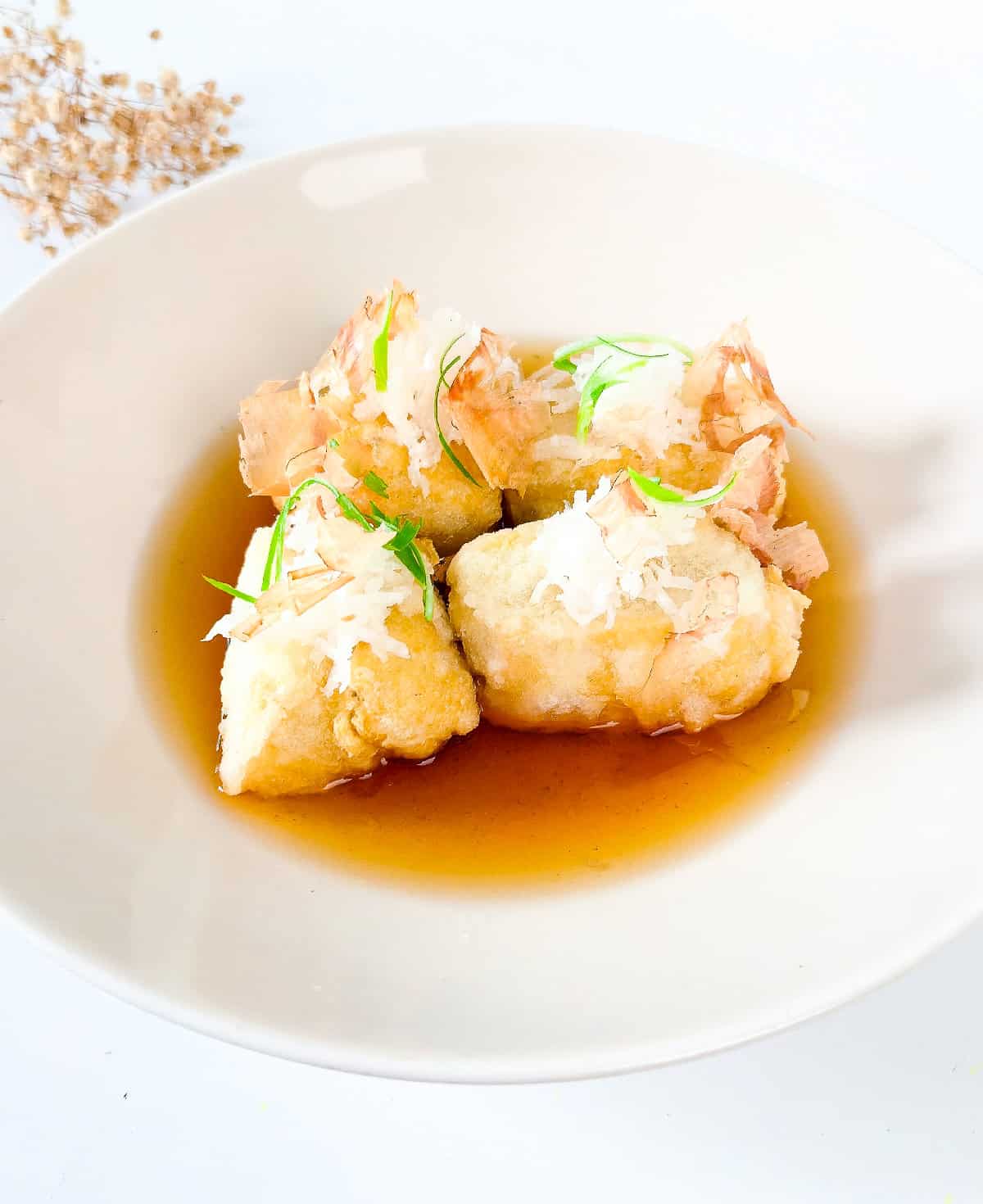 Agedashi tofu served in a light dashi sauce, topped with grated daikon, bonito flakes, and sliced green onions.