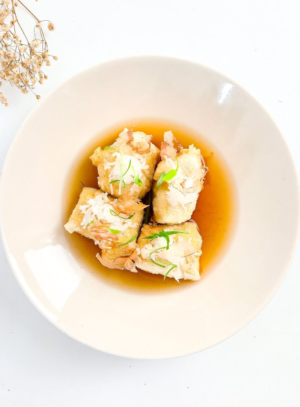 Top view of agedashi tofu garnished with bonito flakes and green onions in dashi broth.