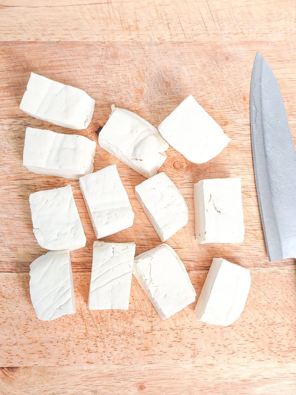 Cutting tofu into evenly sized cubes on a wooden cutting board.