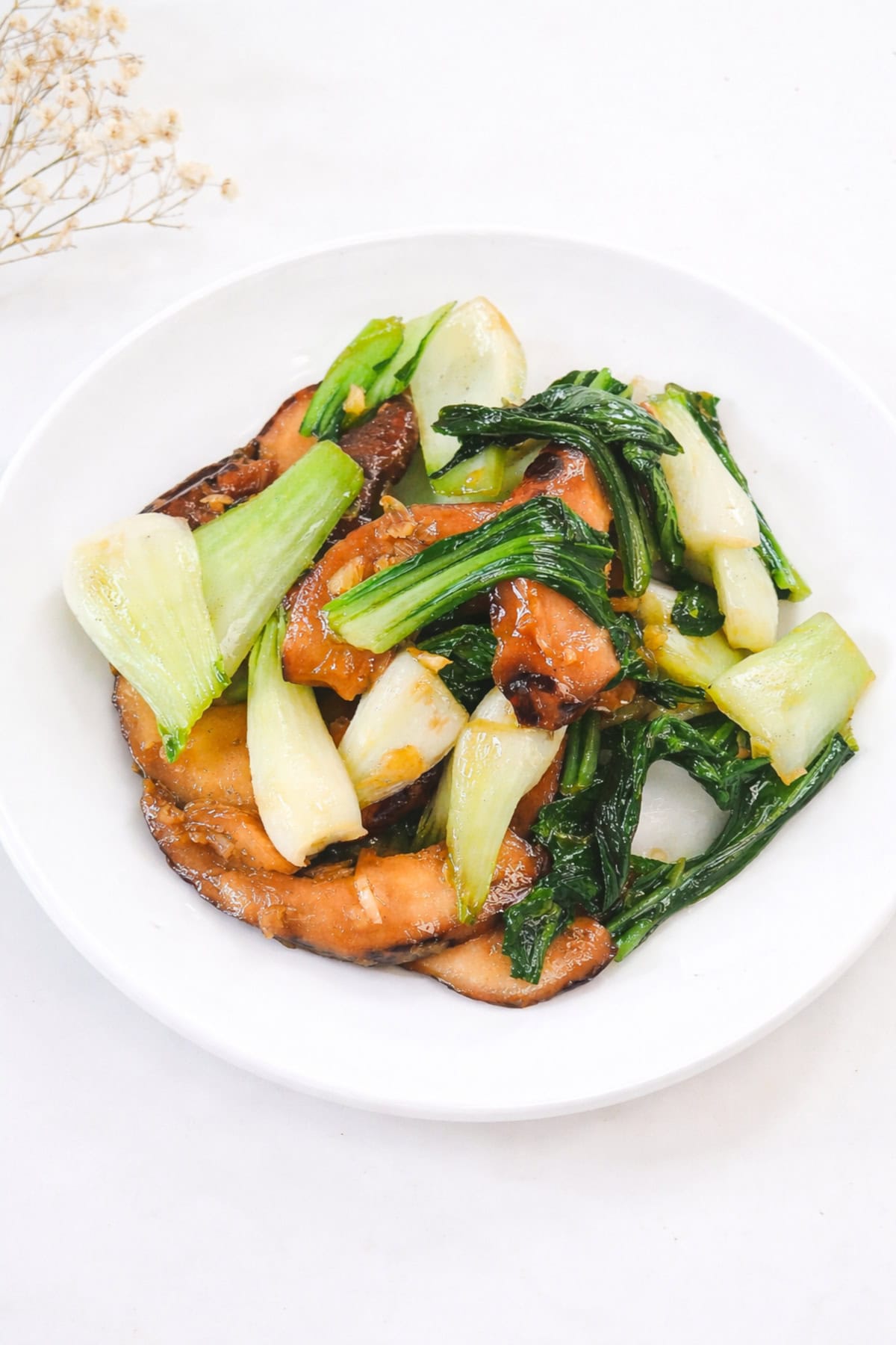 Stir-fried bok choy with shiitake mushrooms served in a white bowl on a light background.