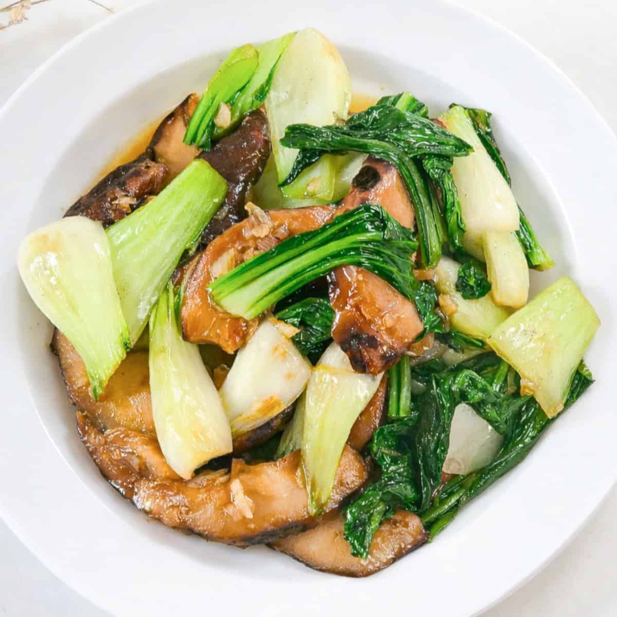 Bok choy mushroom stir fry with tender greens and sliced shiitake mushrooms in a white bowl.