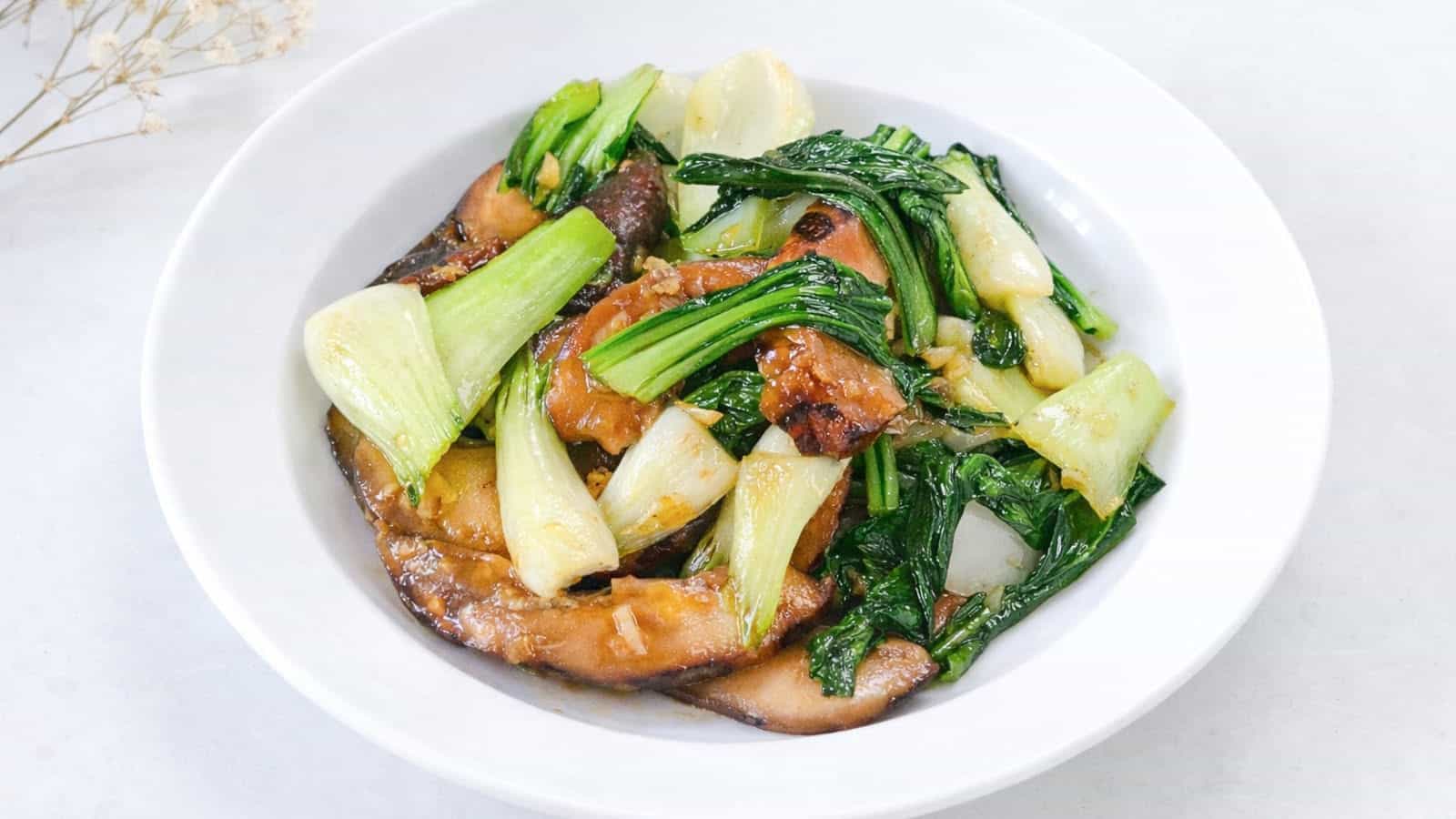 Stir fried bok choy with shiitake mushrooms served in a white bowl on a light background.