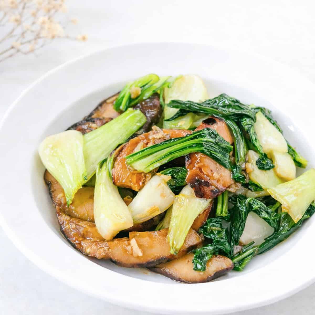 Asian-style bok choy and mushroom stir fry served in a white bowl on a bright surface.
