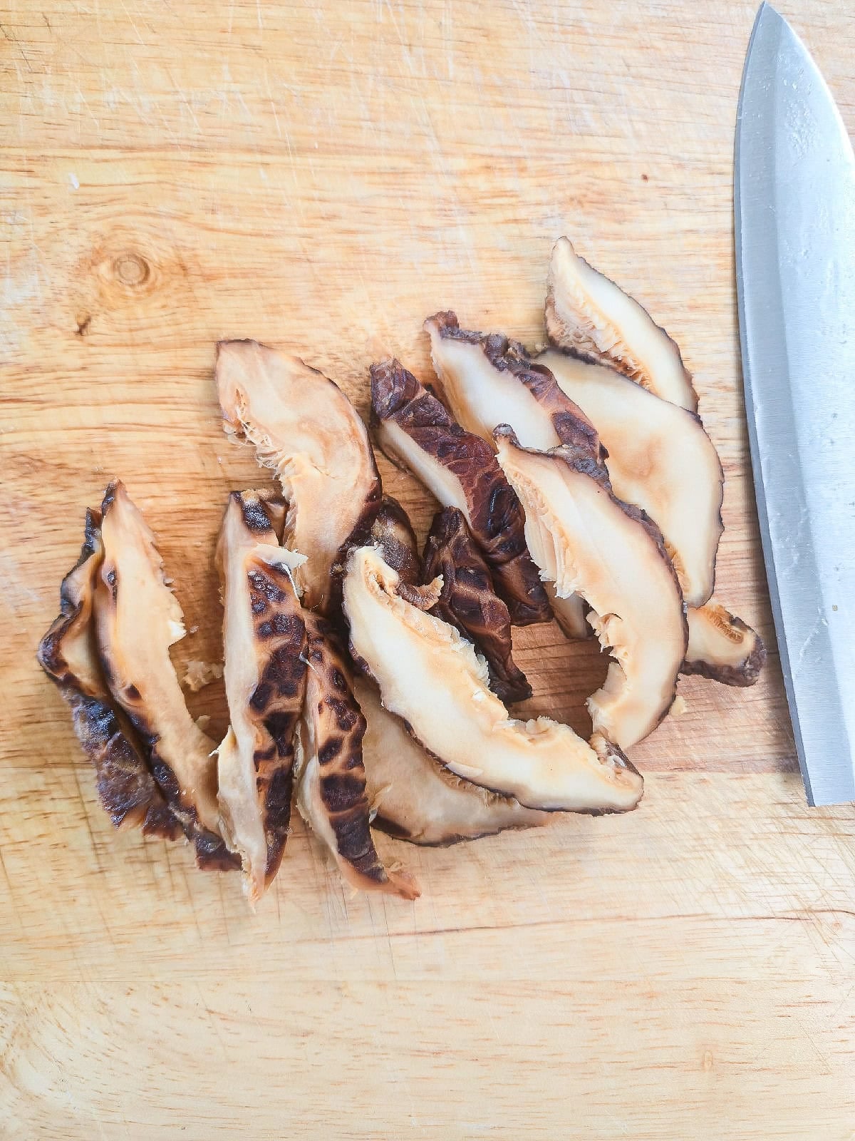 Sliced soaked shiitake mushrooms on a cutting board.