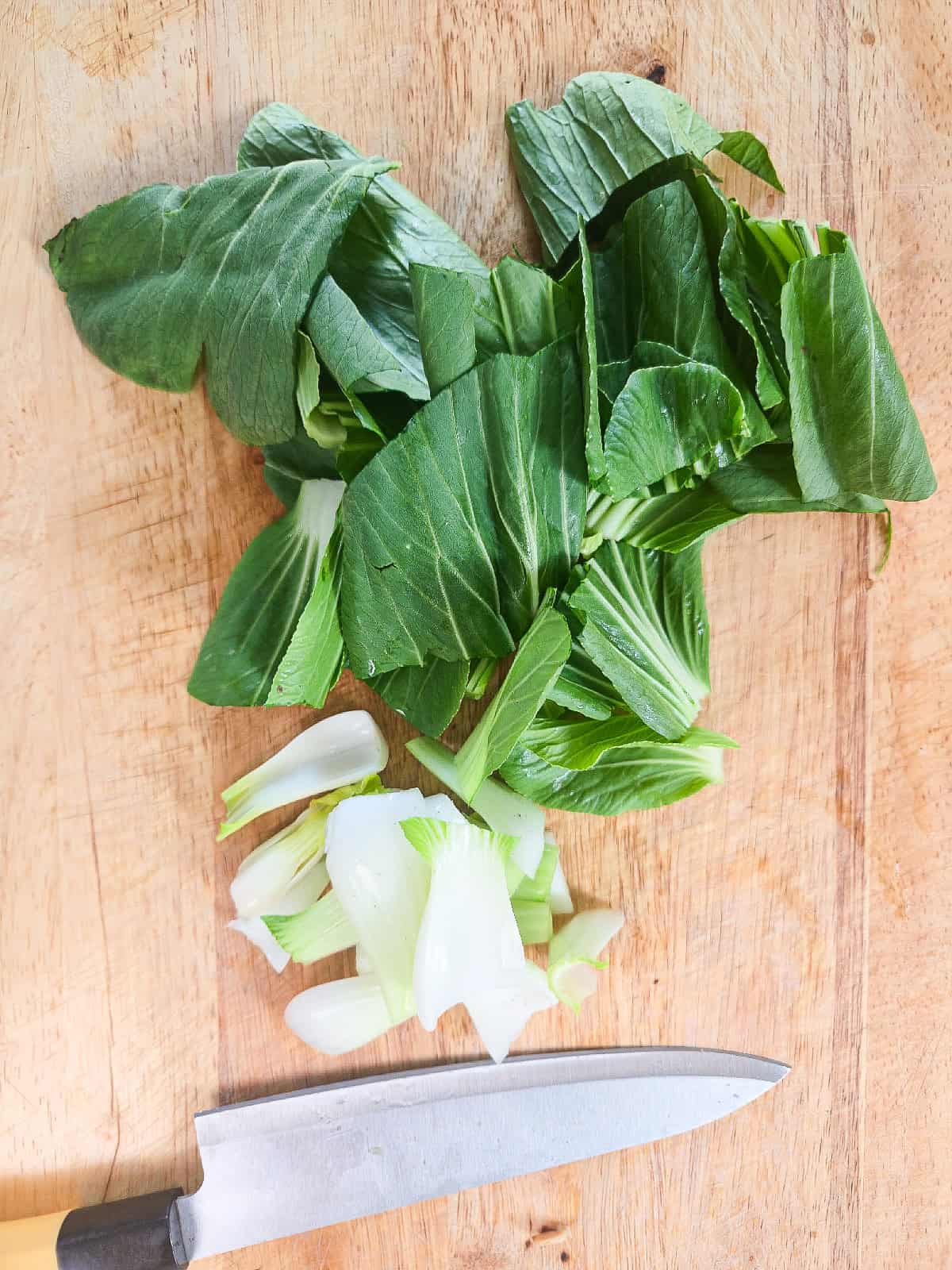 Chopped bok choy stems and leaves separated on a cutting board.