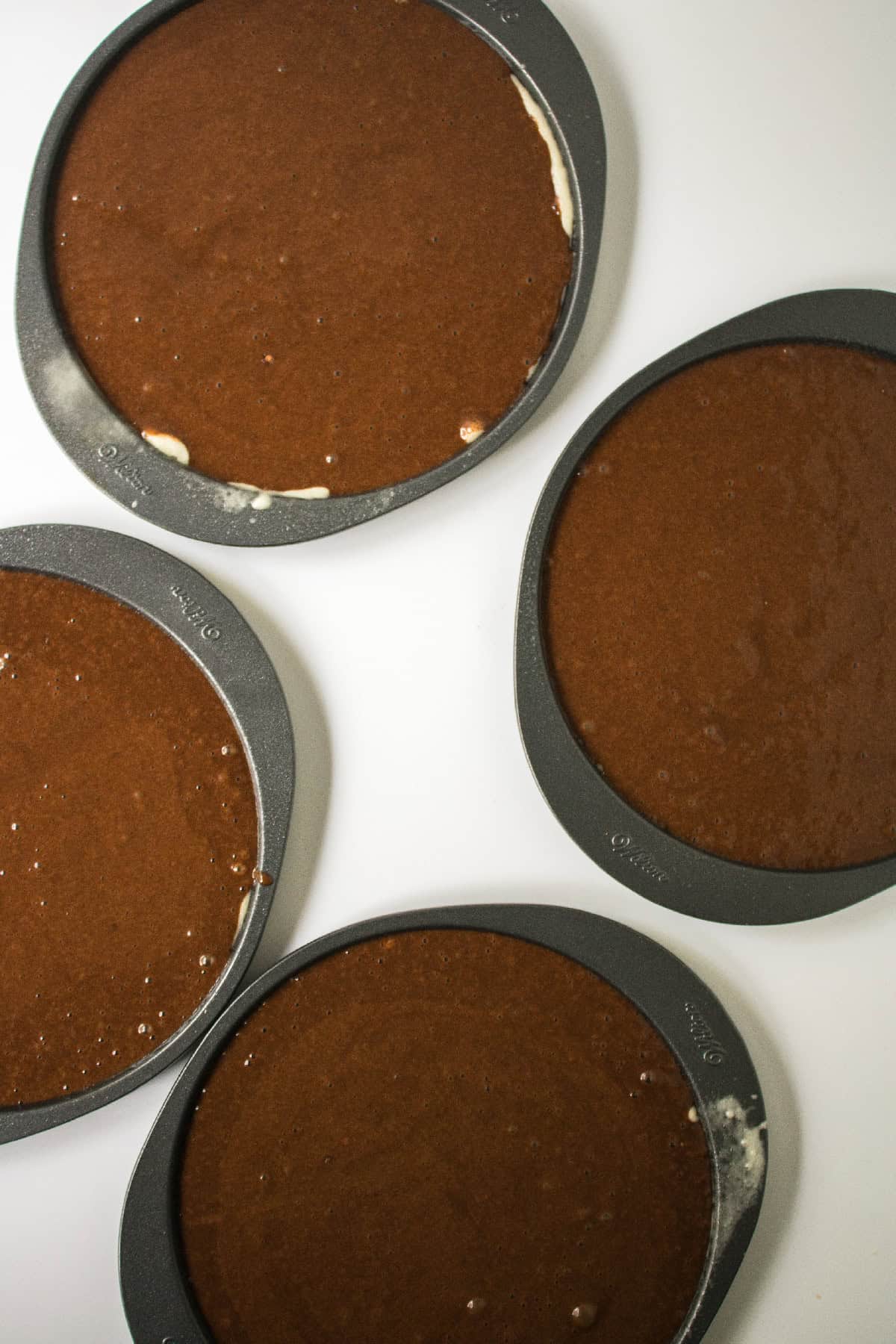 Chocolate cake batter evenly divided into round cake pans ready for baking.