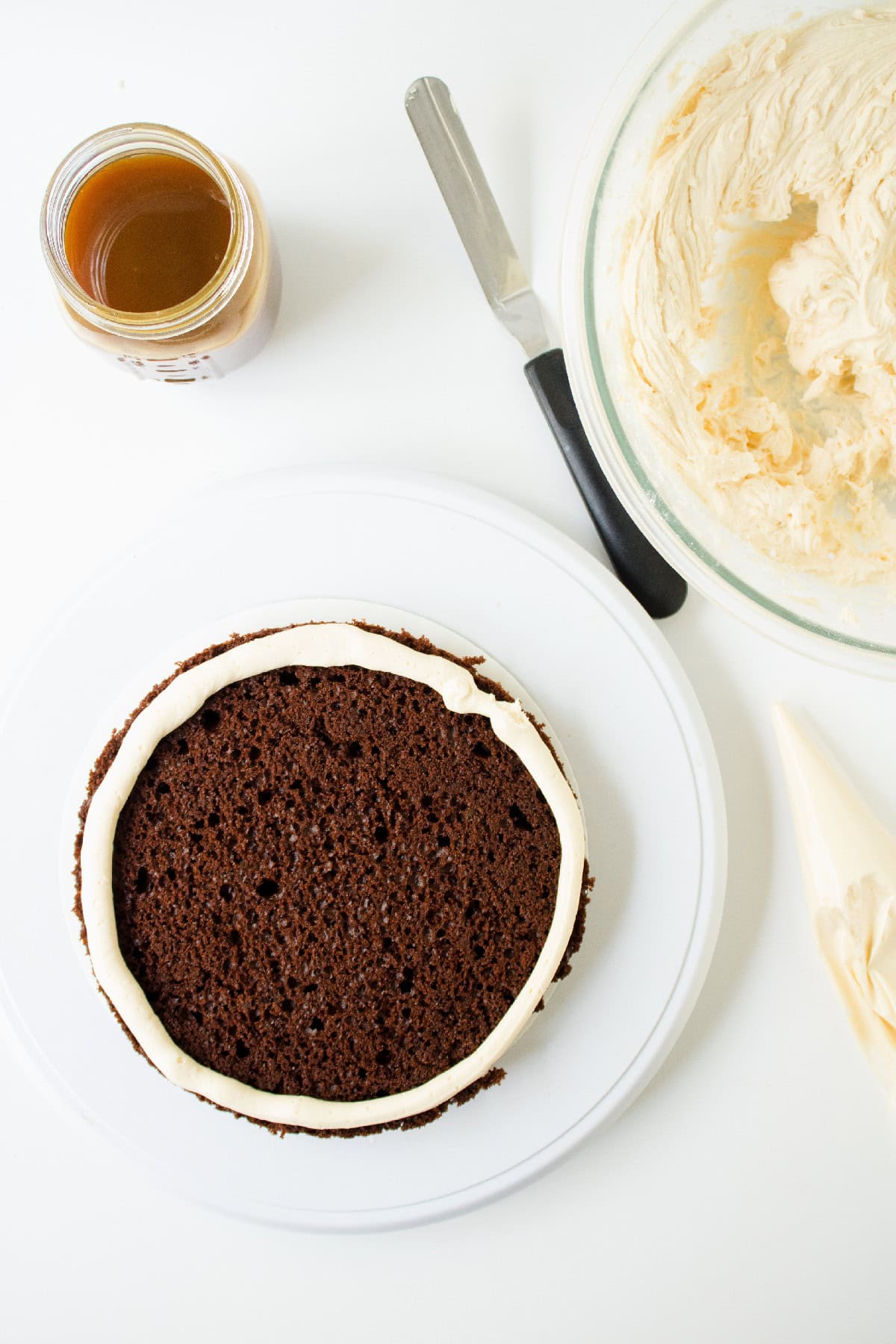 Chocolate cake layer piped with a buttercream border on a white cake plate.