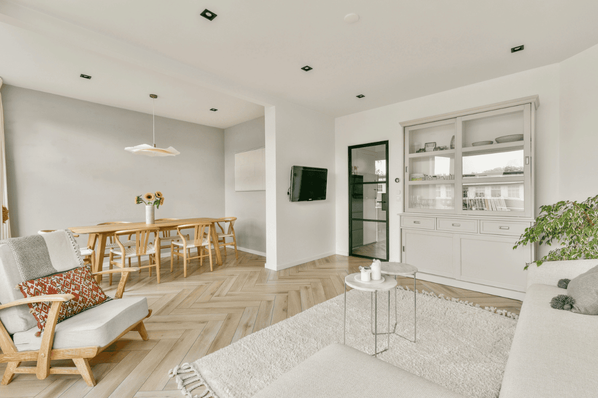 Minimalist living and dining area with light wood furniture, neutral tones, and herringbone floors.