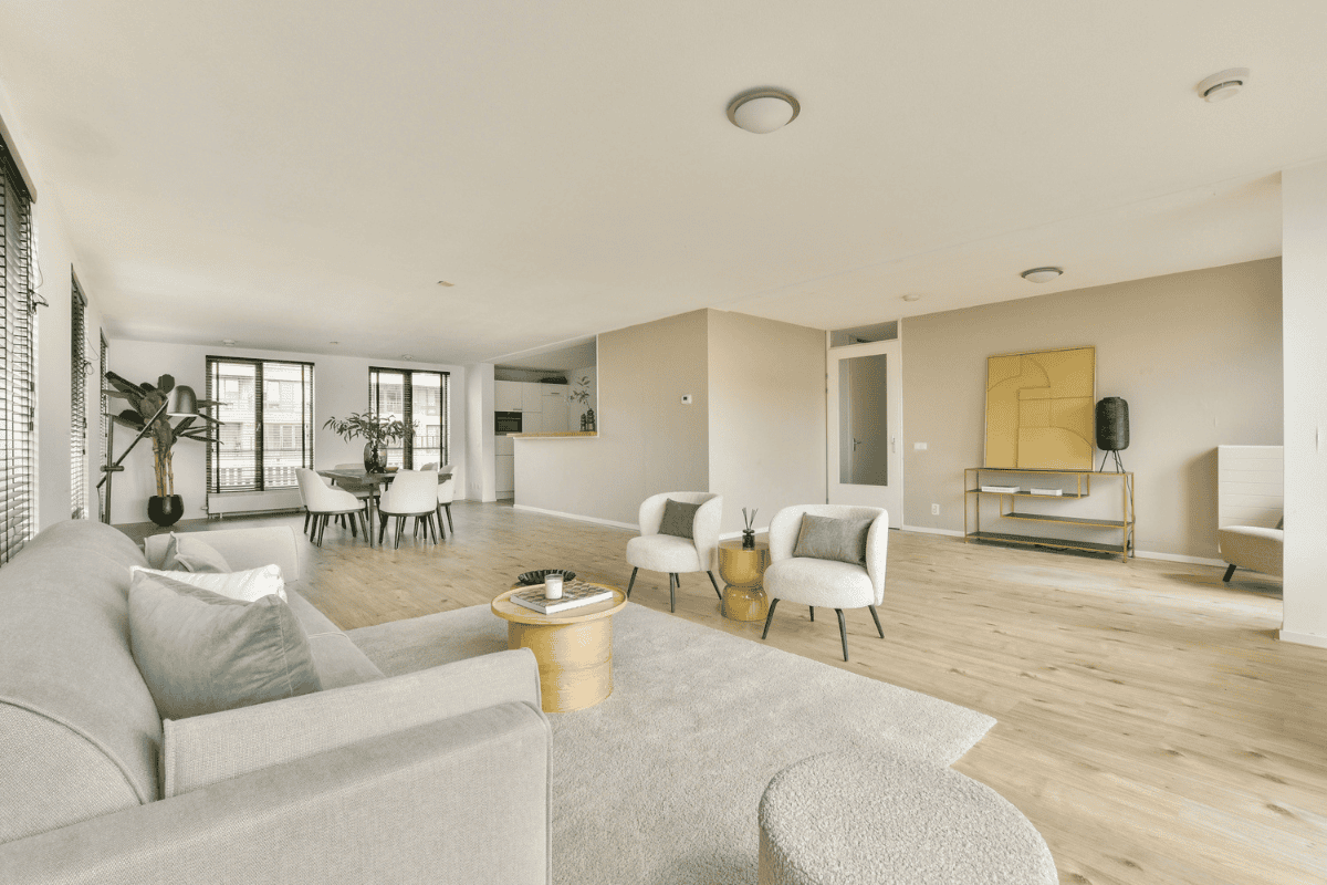 Minimalist open-plan living and dining area with neutral furniture, light wood floors, and large windows.