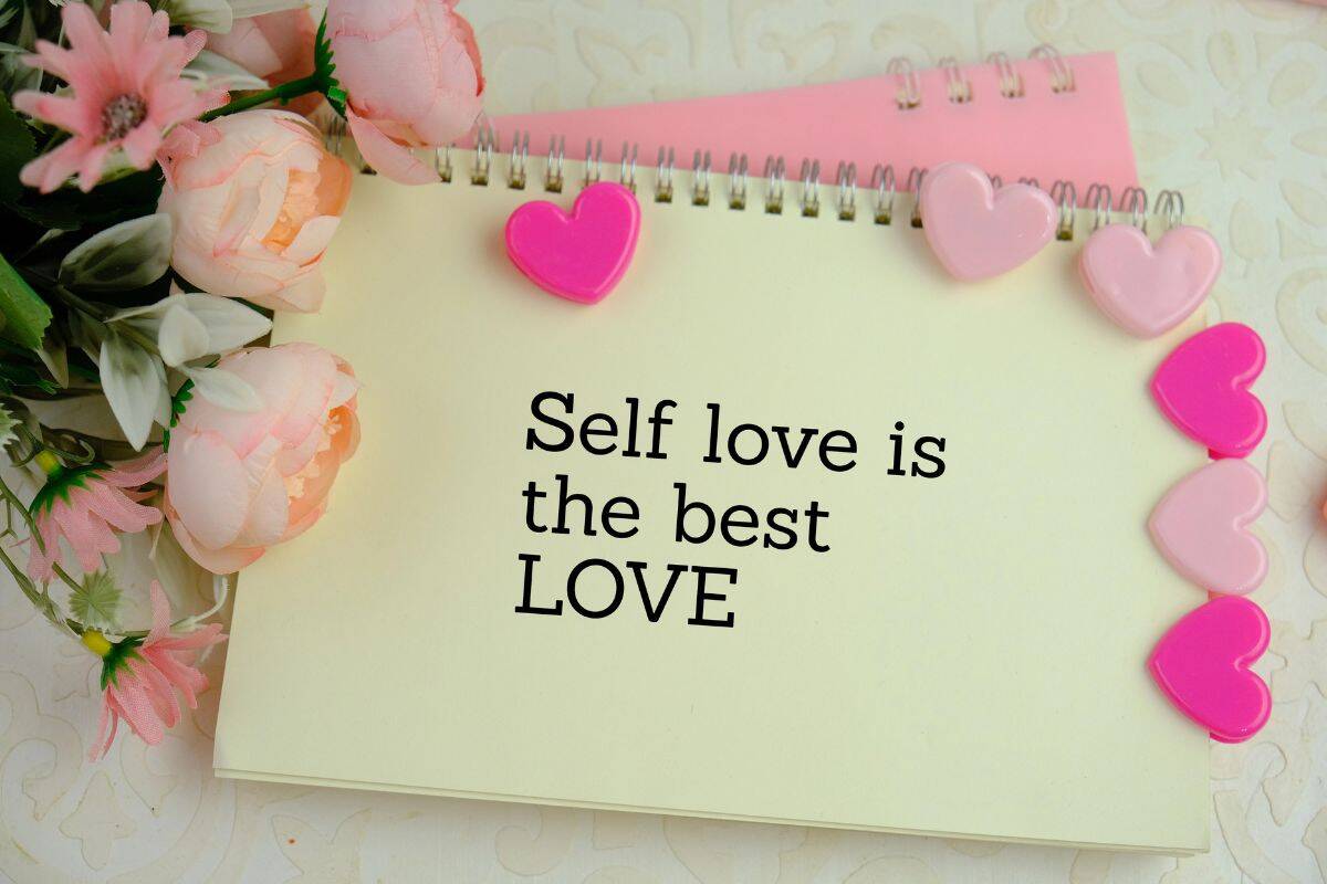 Notebook with the message “Self love is the best love,” decorated with pink heart shapes and flowers.