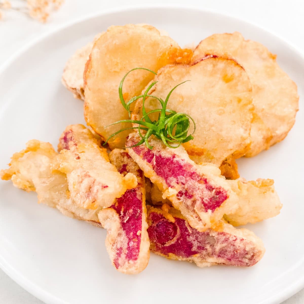 Crispy sweet potato tempura with purple-skinned slices on a white plate, garnished with green onions.