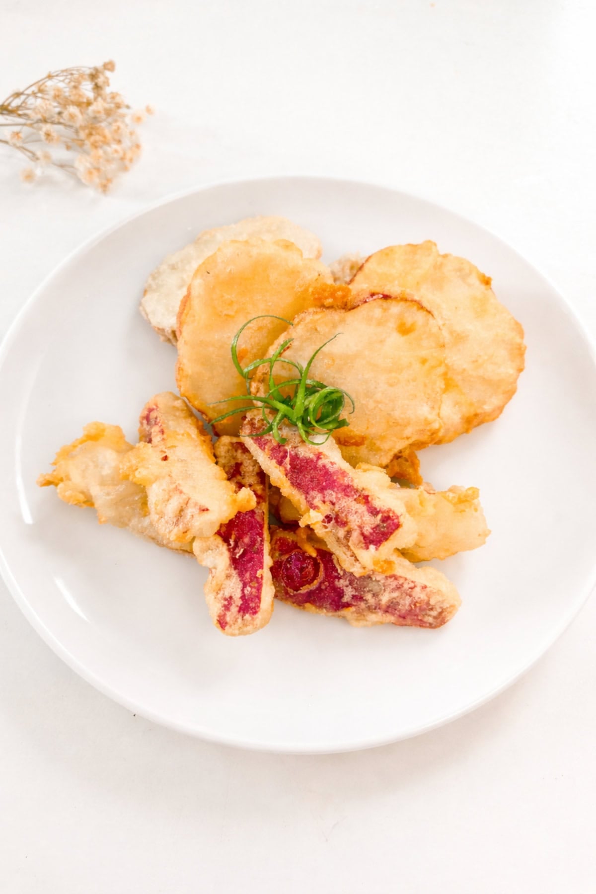 Japanese sweet potato tempura stacked on a white plate with a light, airy batter.