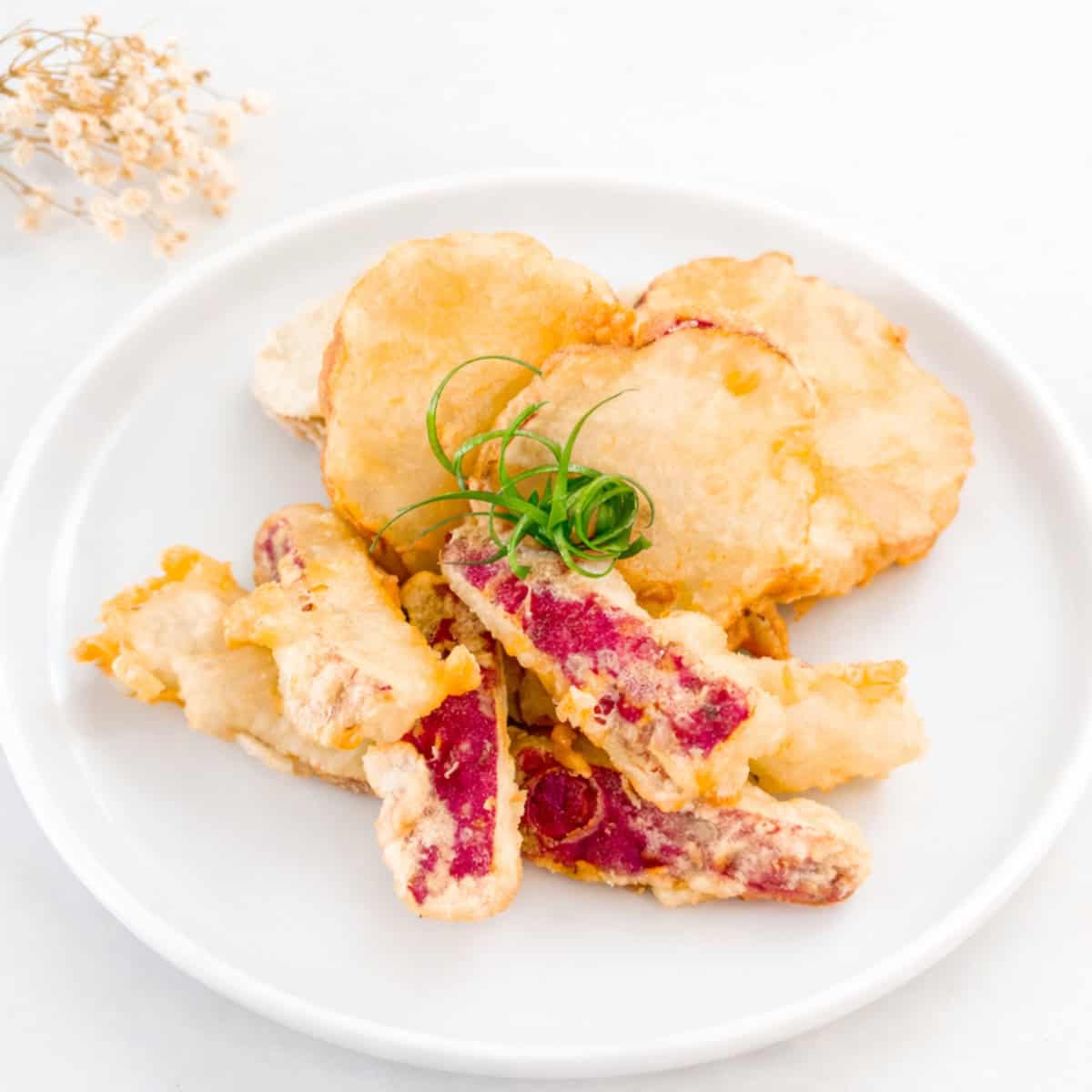 Sweet potato tempura pieces served on a white plate with a crisp, delicate coating.