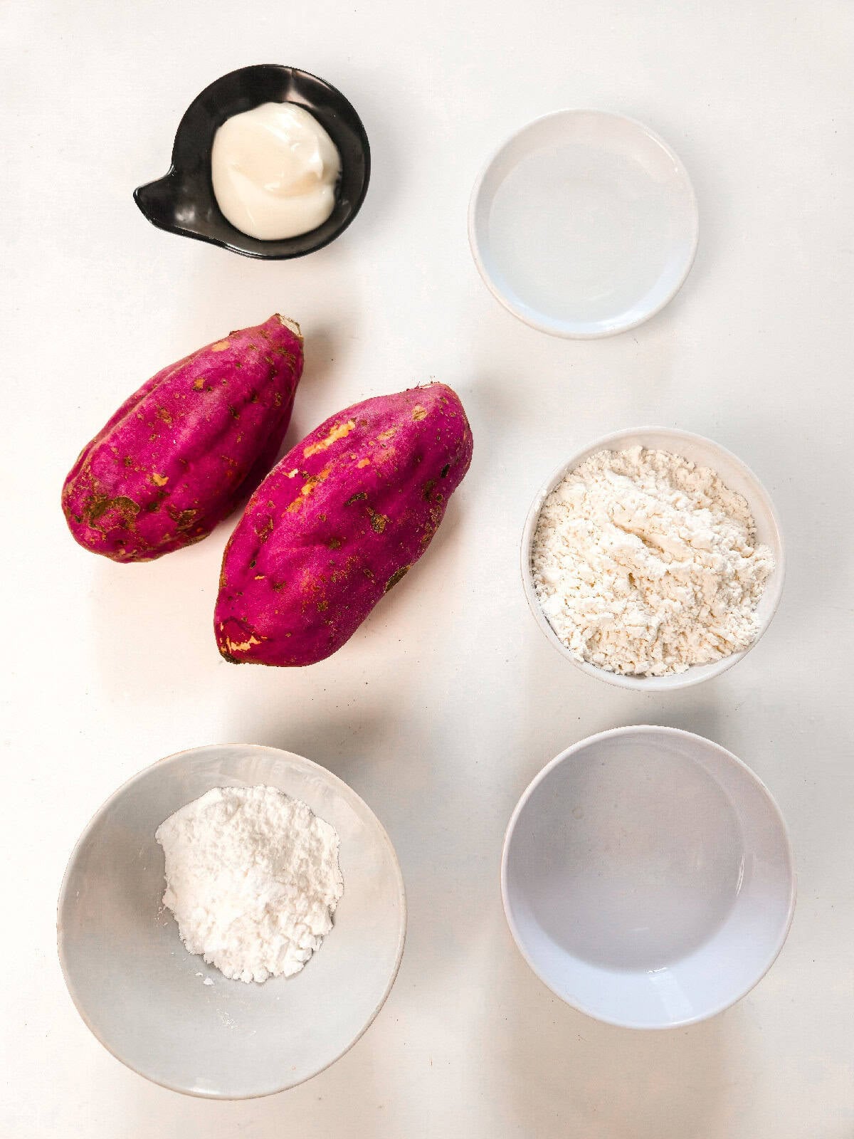 Sweet potato tempura ingredients arranged on a white surface, including whole sweet potatoes, flour, cornstarch, cold water, and mayonnaise.