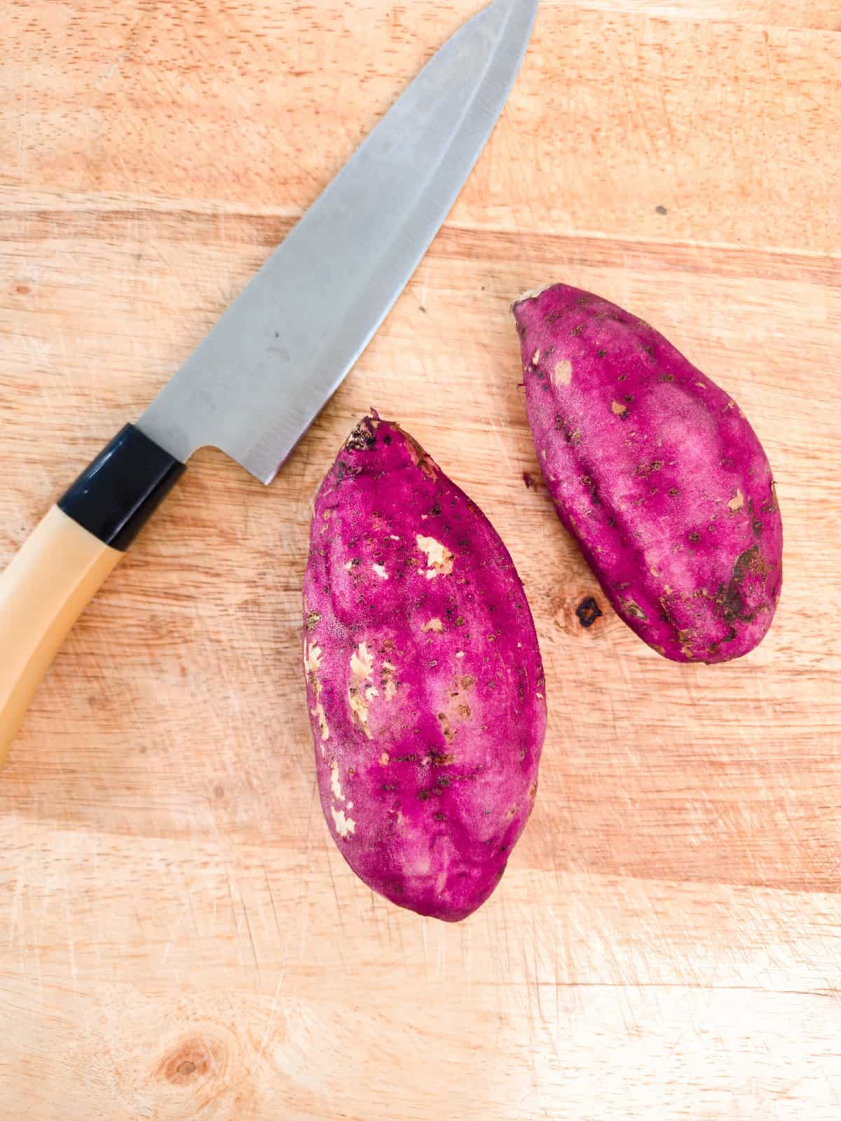 Whole purple sweet potatoes on a cutting board with a kitchen knife.