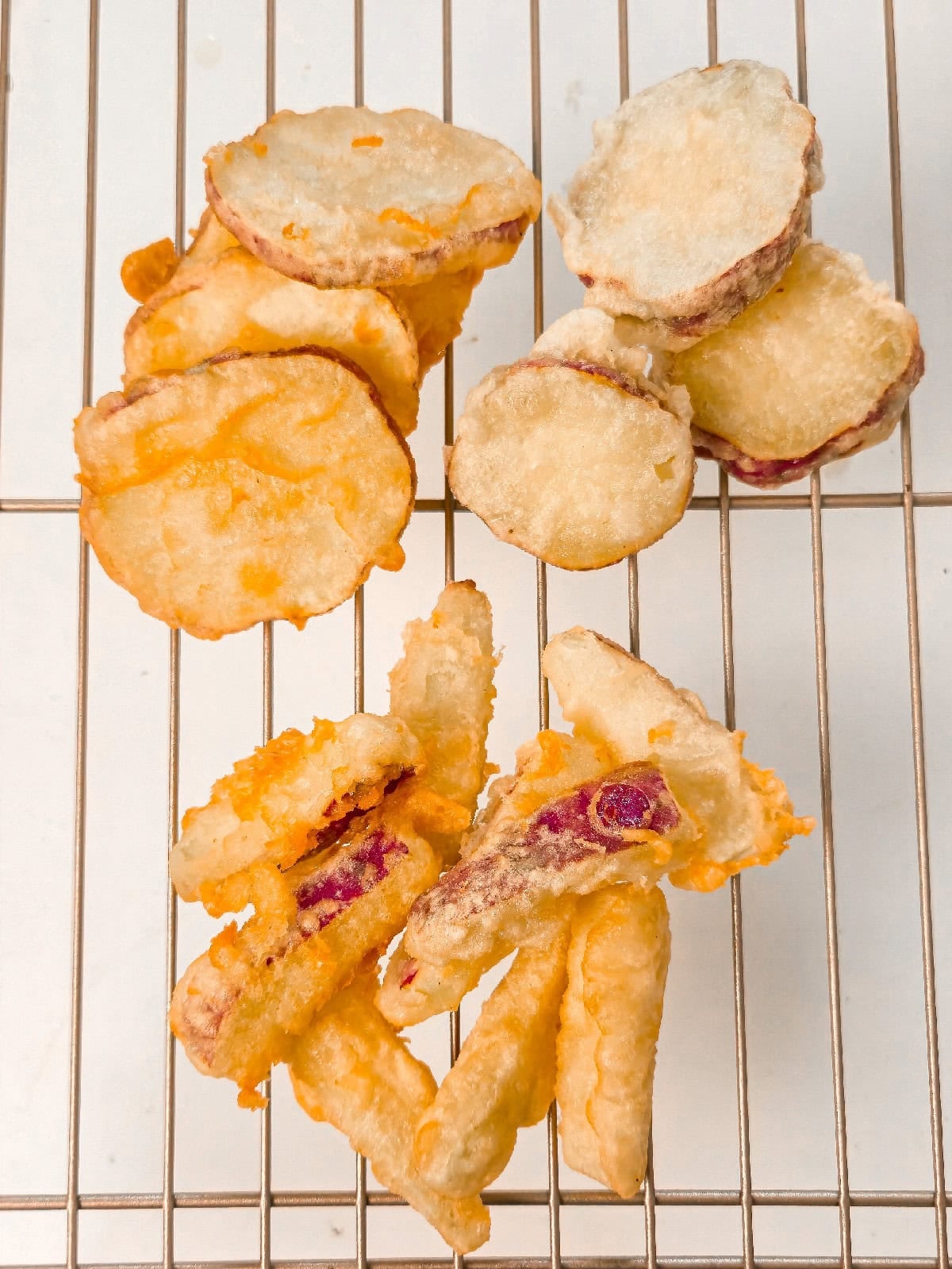 Crispy sweet potato tempura draining on a wire rack after frying, showing golden batter and tender centers.