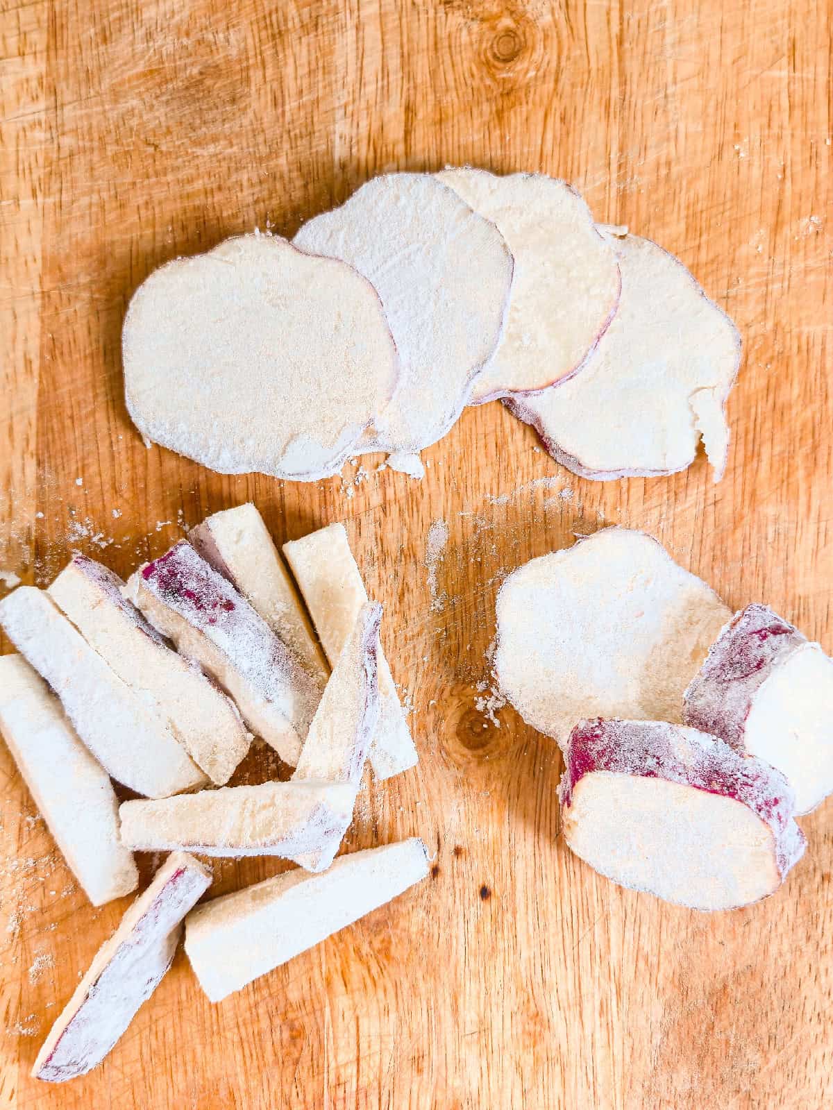 Thinly sliced sweet potatoes coated lightly in flour, prepared for making sweet potato tempura on a wooden cutting board.