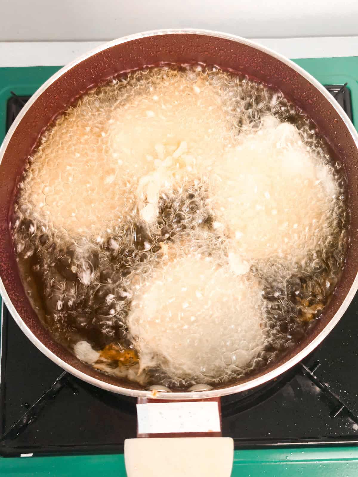 Sweet potato slices frying in hot oil, bubbling as the tempura coating crisps up in a saucepan.