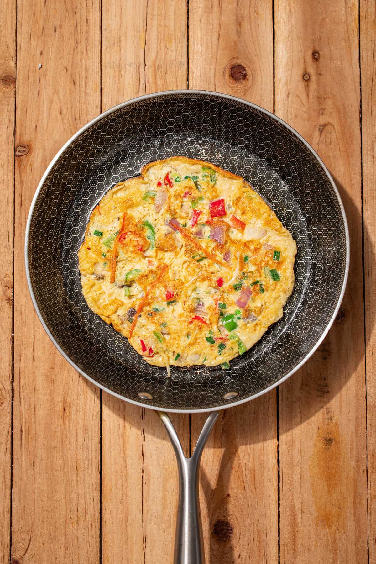 Vegetable egg foo young omelet cooking in a skillet until golden and set.