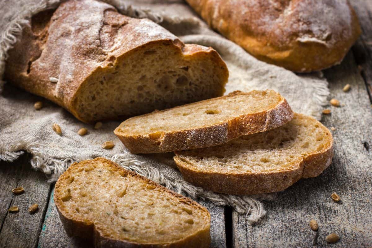 Sliced rustic whole wheat bread loaf on a wooden surface with visible grain texture.