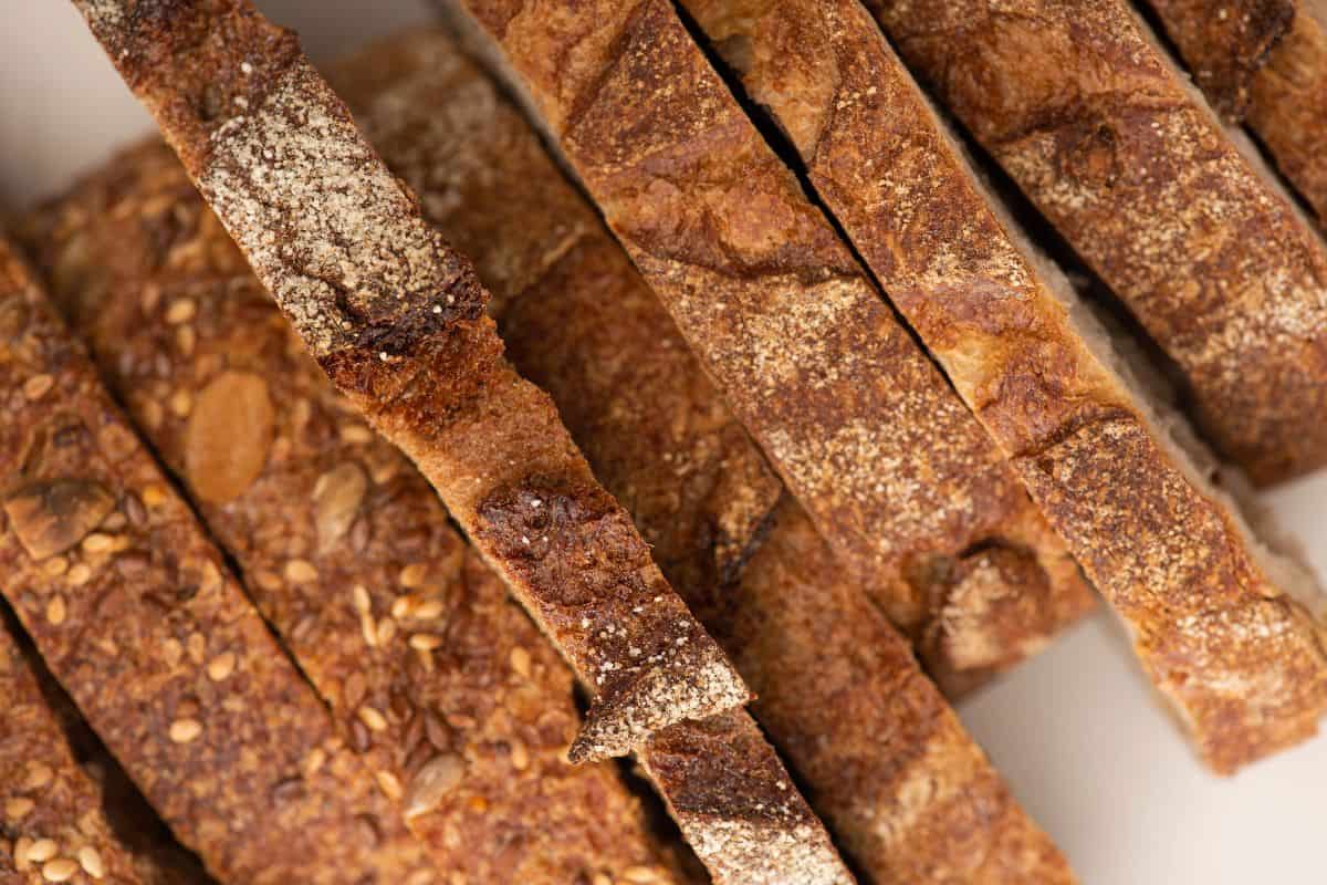 Assorted whole grain bread slices with seeds and crusty texture stacked together.
