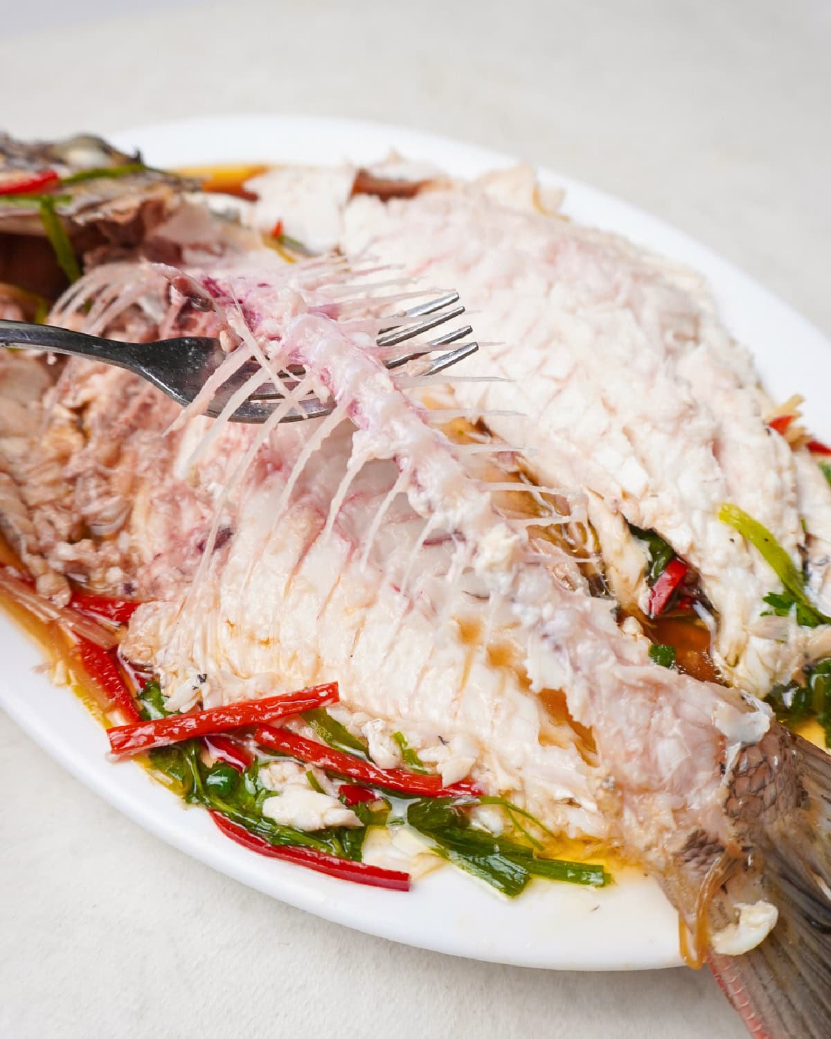 Fresh steamed fish with herbs and chili on a white plate, ready to serve.