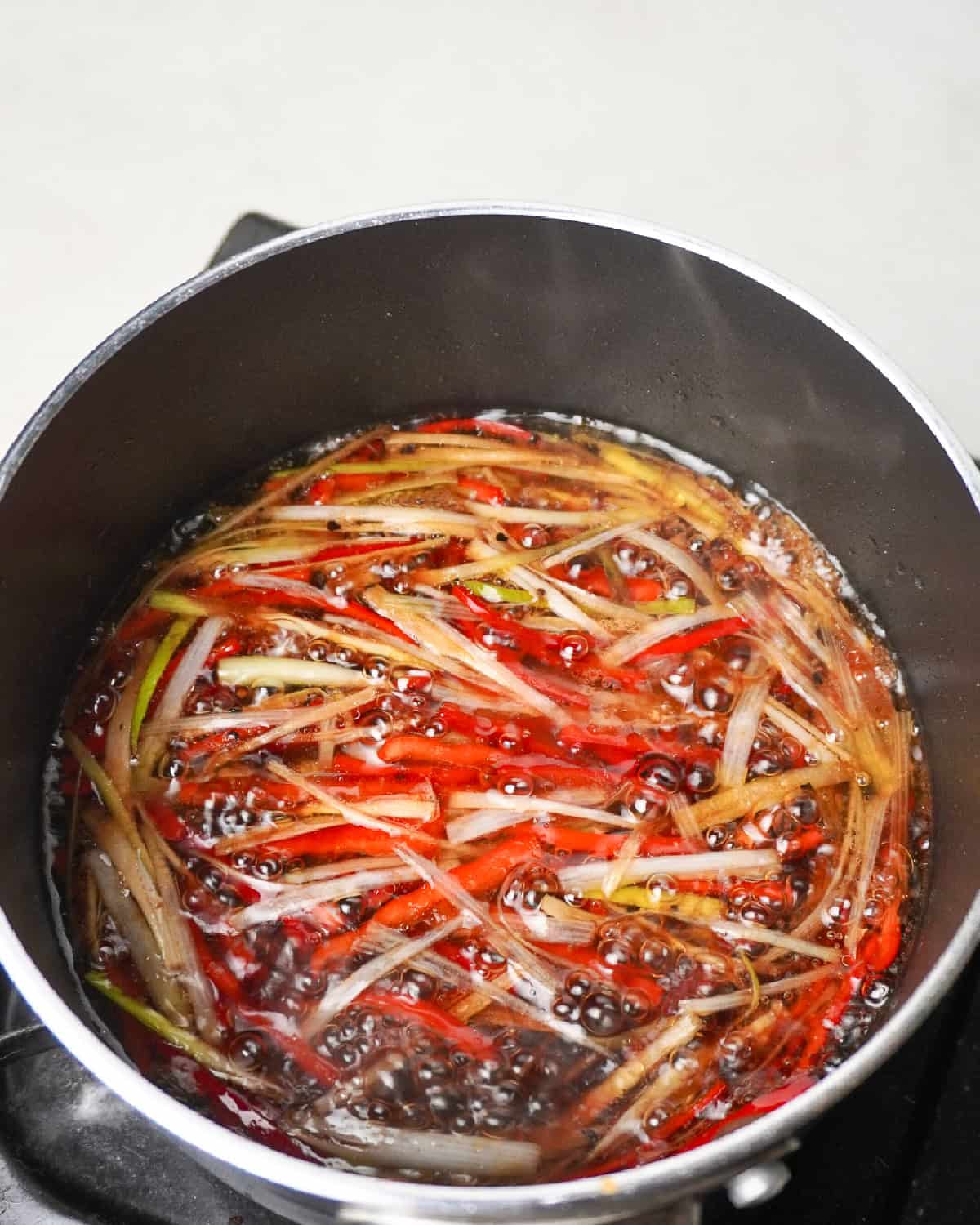 Simmering soy sauce with ginger, scallions, and red chili for Chinese steamed bass.