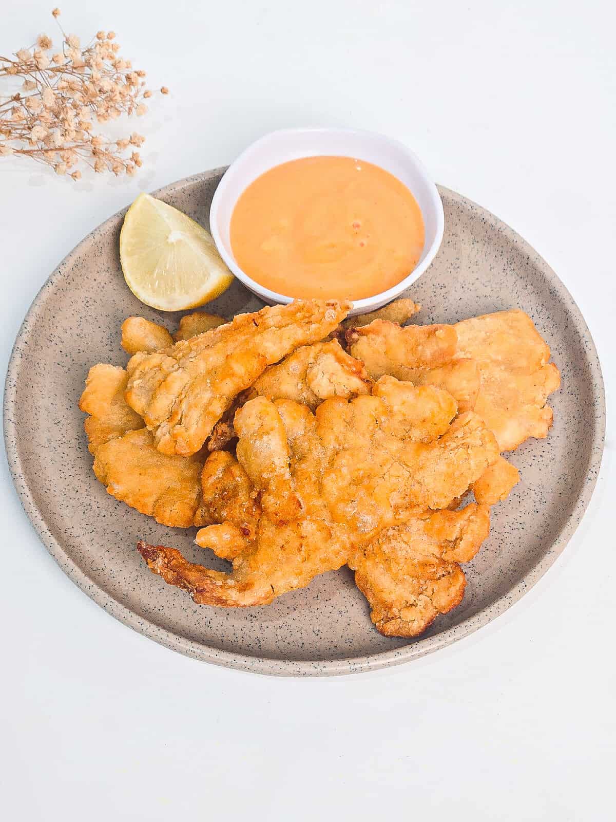 Top-down view of golden air fryer oyster mushrooms with dipping sauce and lemon on a ceramic plate.
