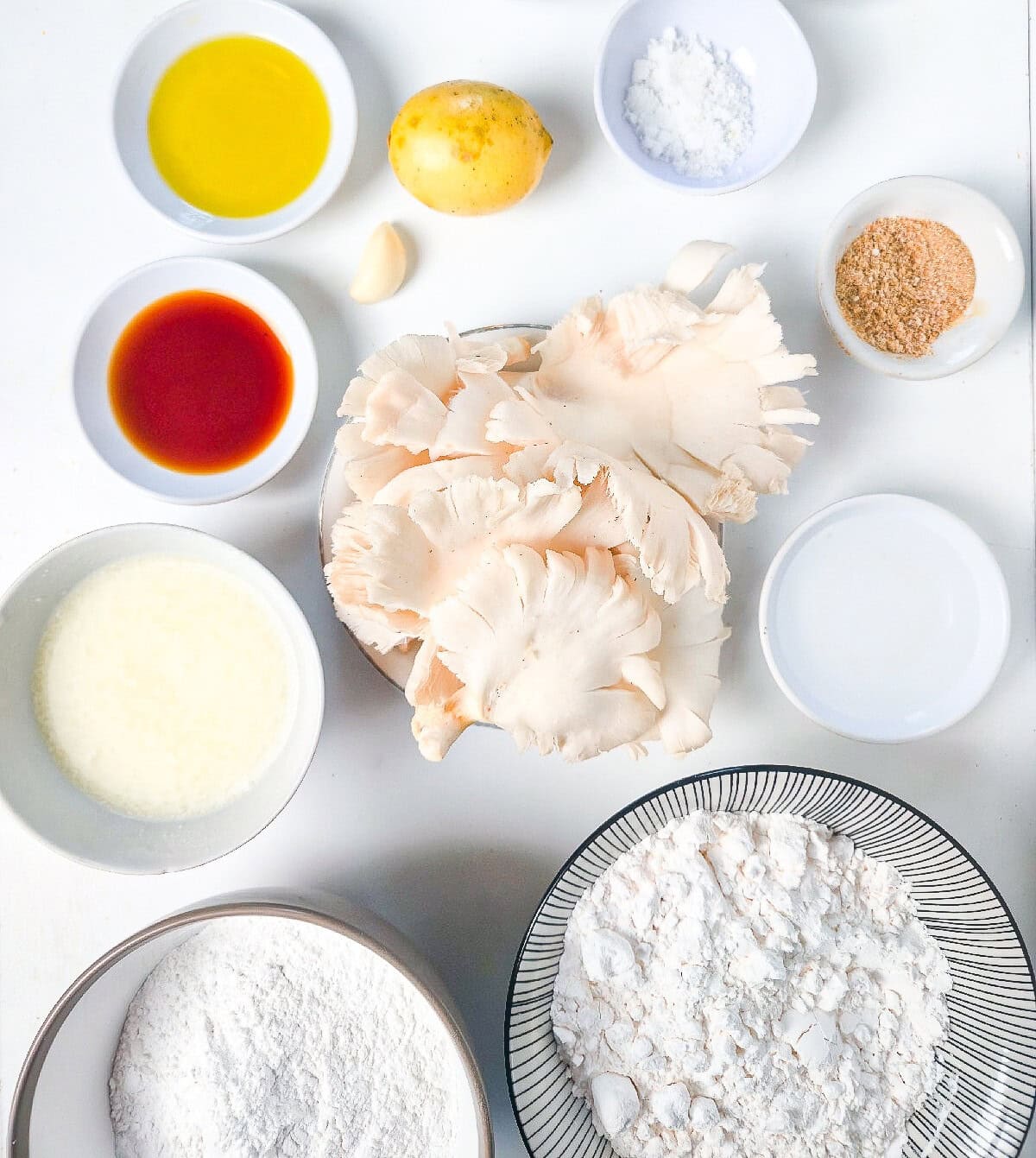 Air fryer oyster mushroom ingredients arranged on a white surface, including oyster mushrooms, oil, spices, lemon, garlic, and starch.